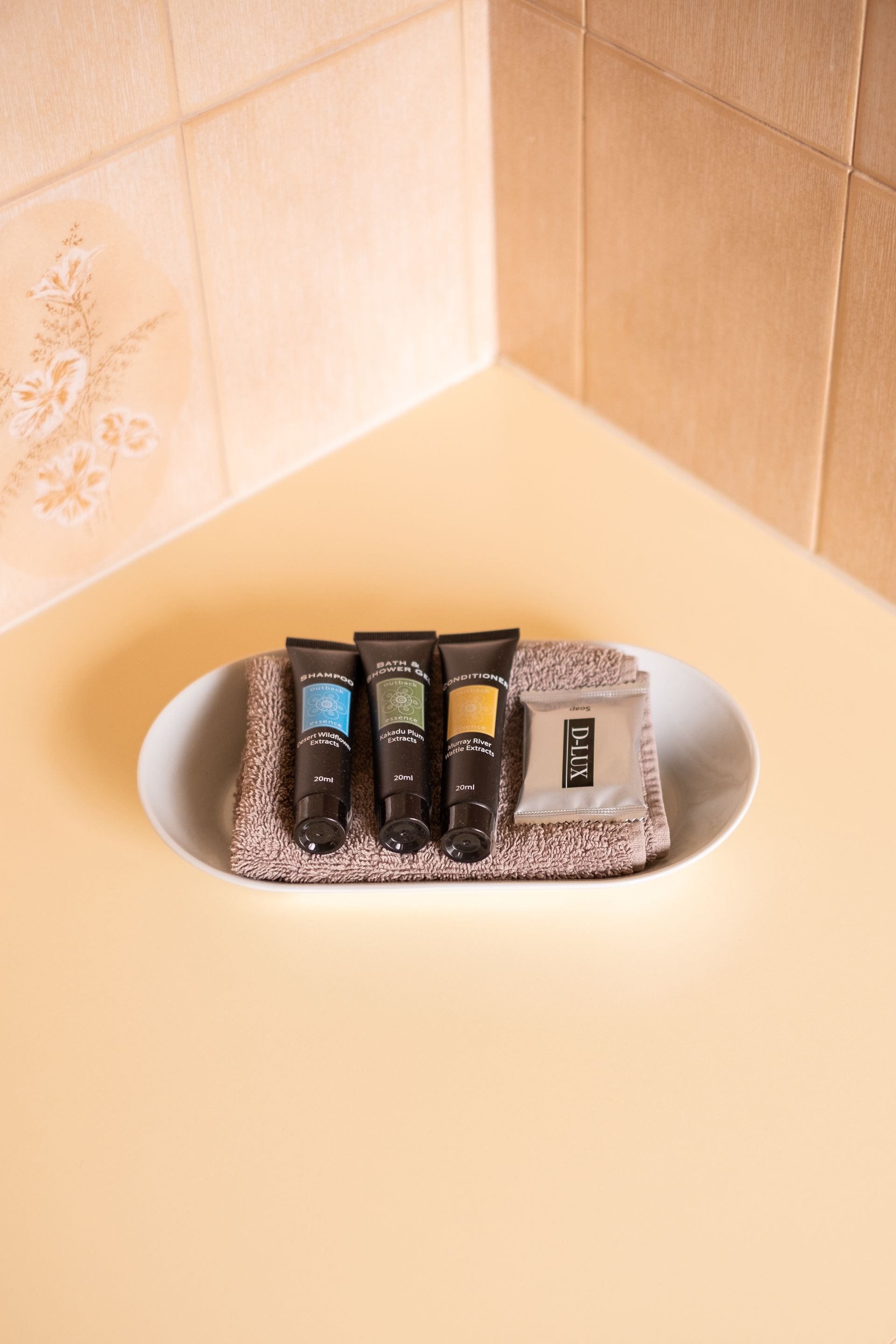 Toiletries in a white oval tray on a peach-colored surface. Beige tiled corner in the background.