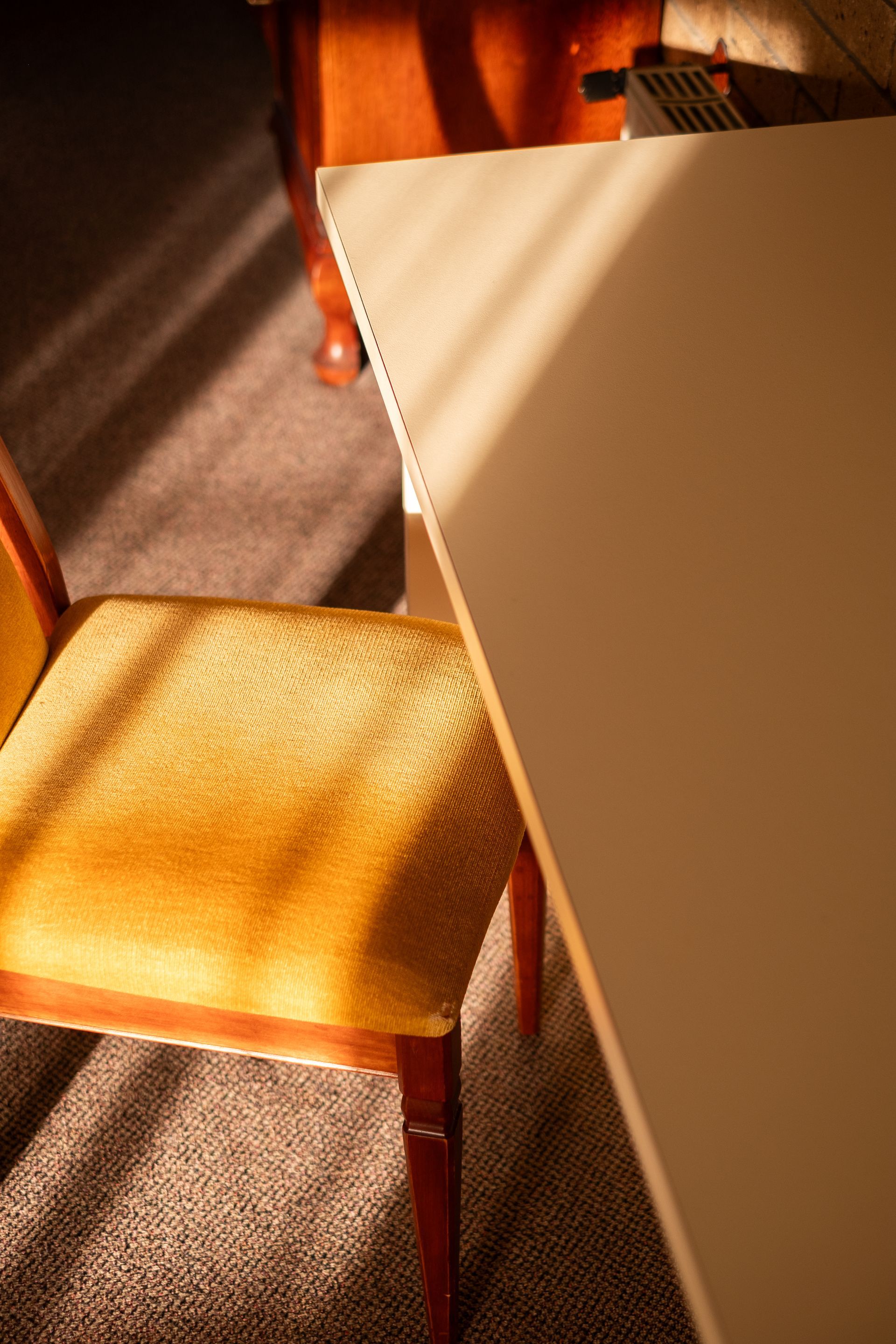 Yellow chair beside a white table corner, sunlight casting shadows on the carpet and furniture.