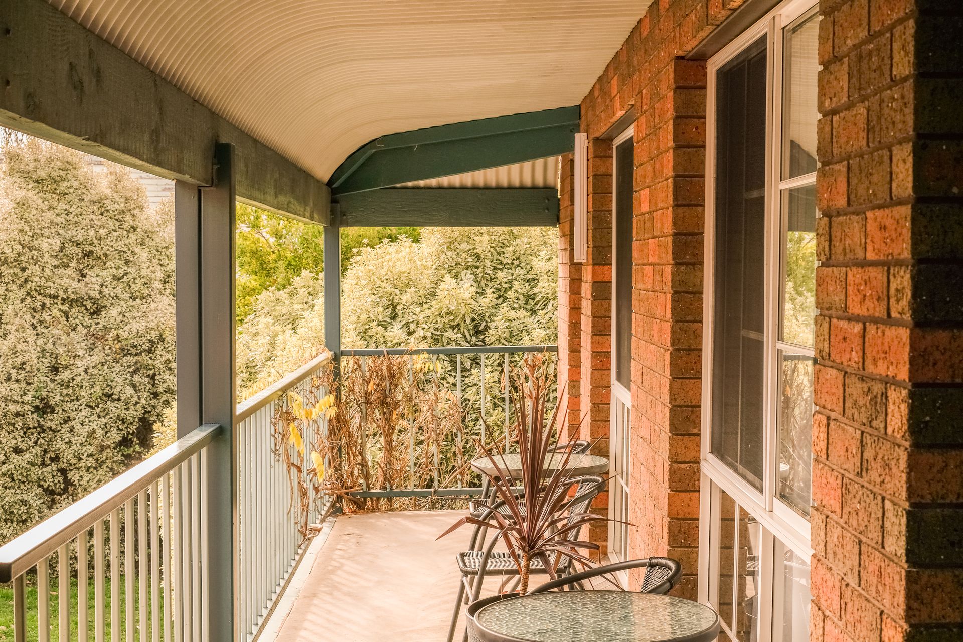 Balcony with brick wall, metal railing and chairs overlooking trees.