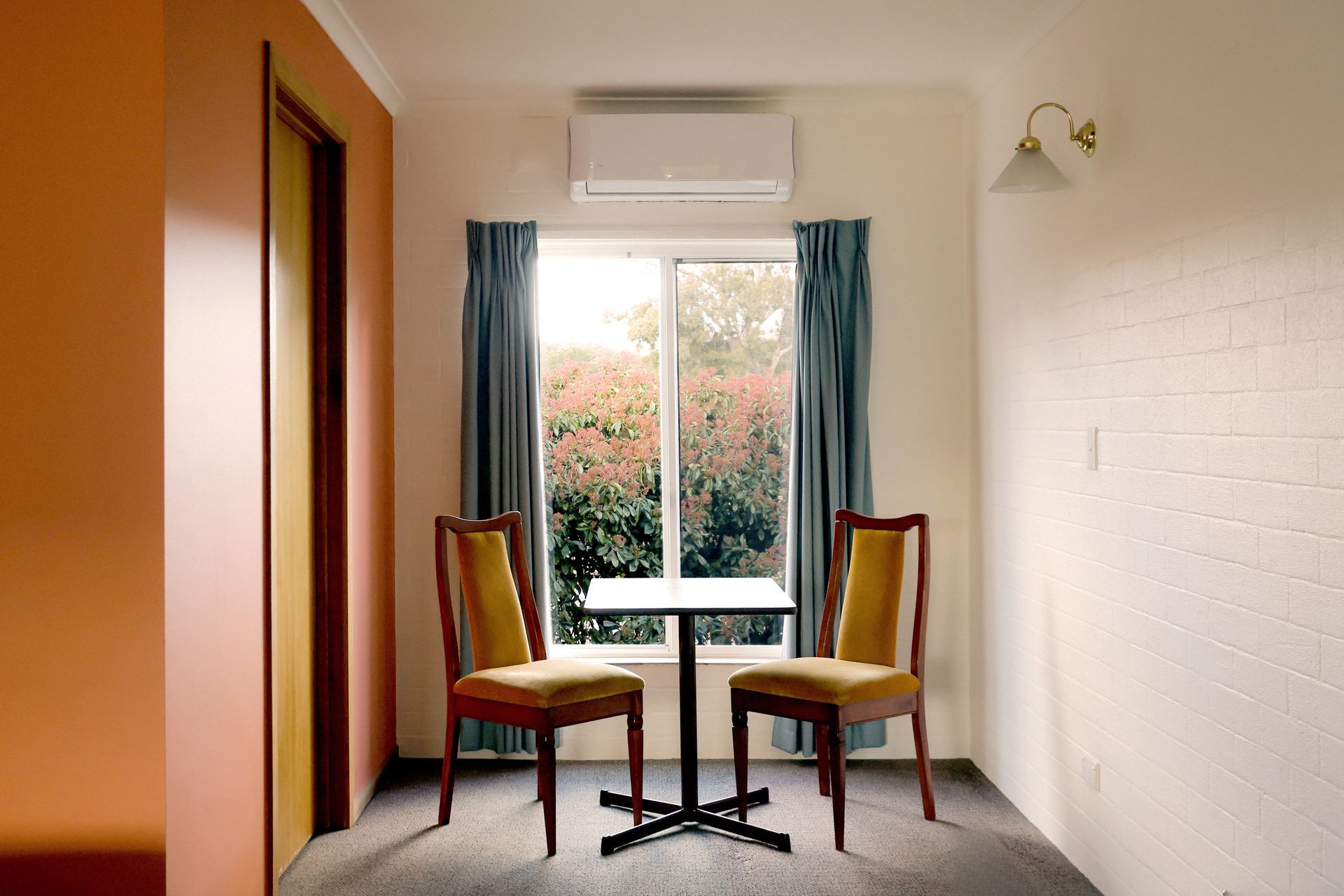 Two chairs and a small table sit by a window with blue curtains. The walls are peach and white.