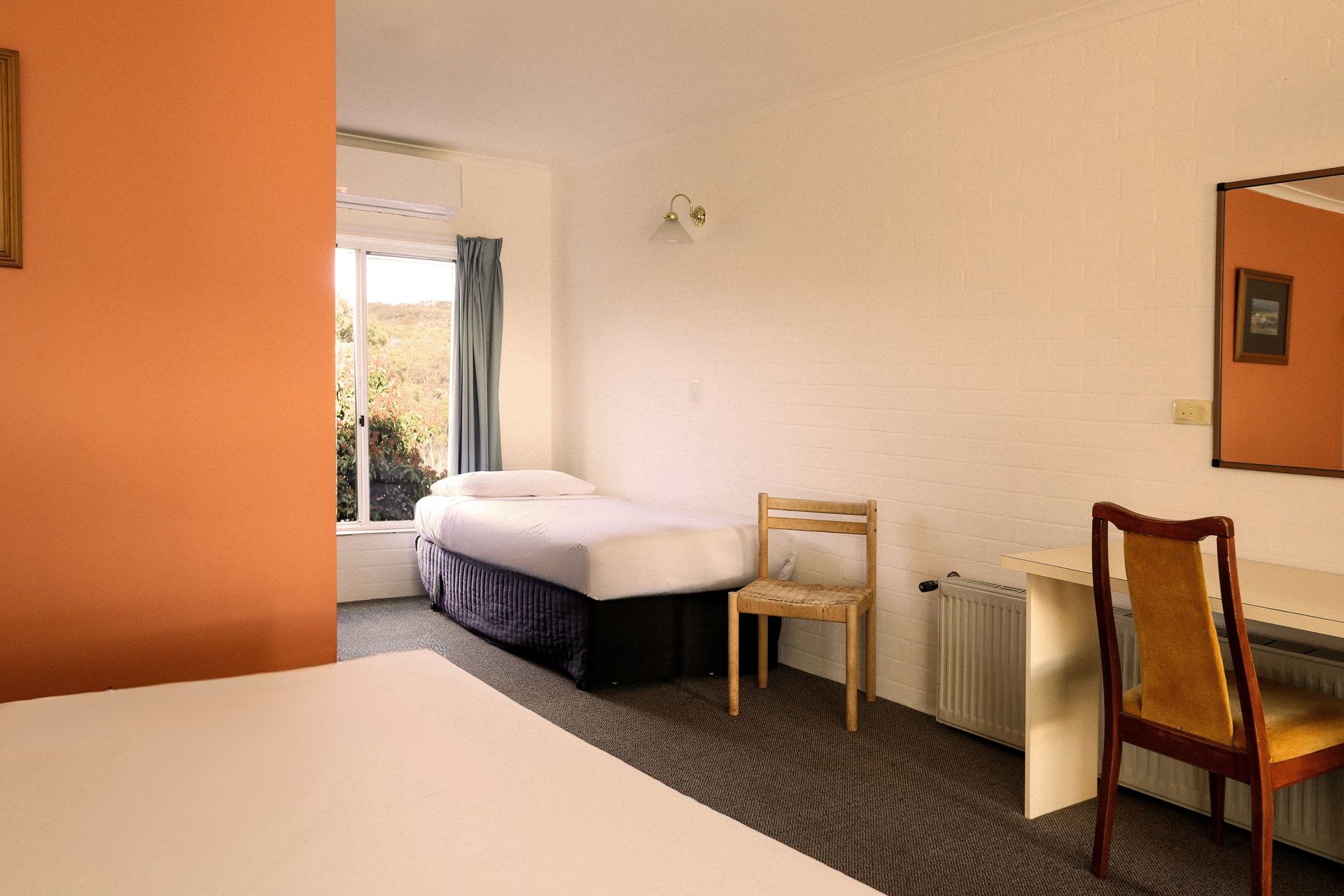 Hotel room with two beds, desk, chair, and an orange accent wall.