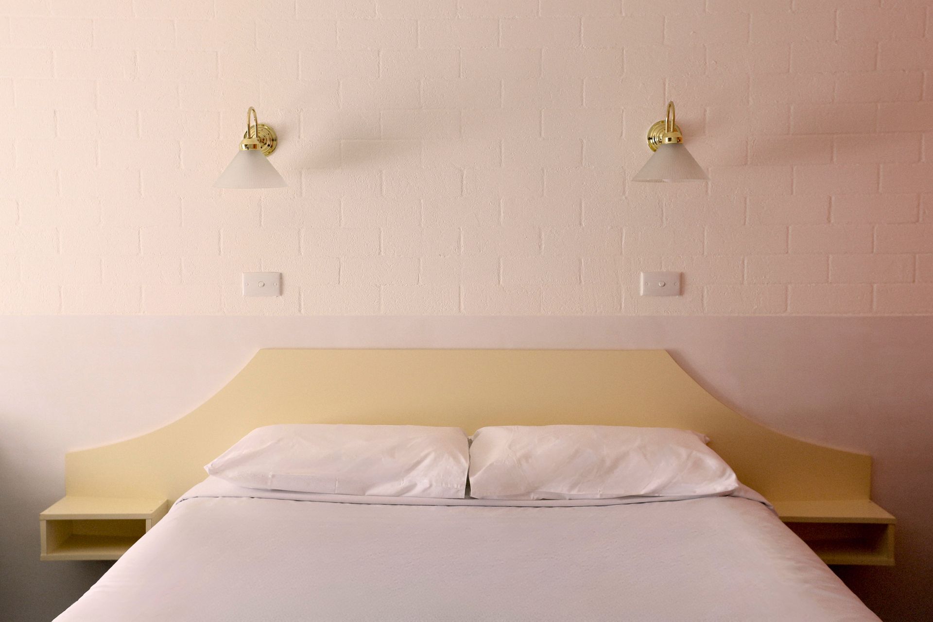 A bed with white linens and a yellow headboard, flanked by nightstands and wall sconces.