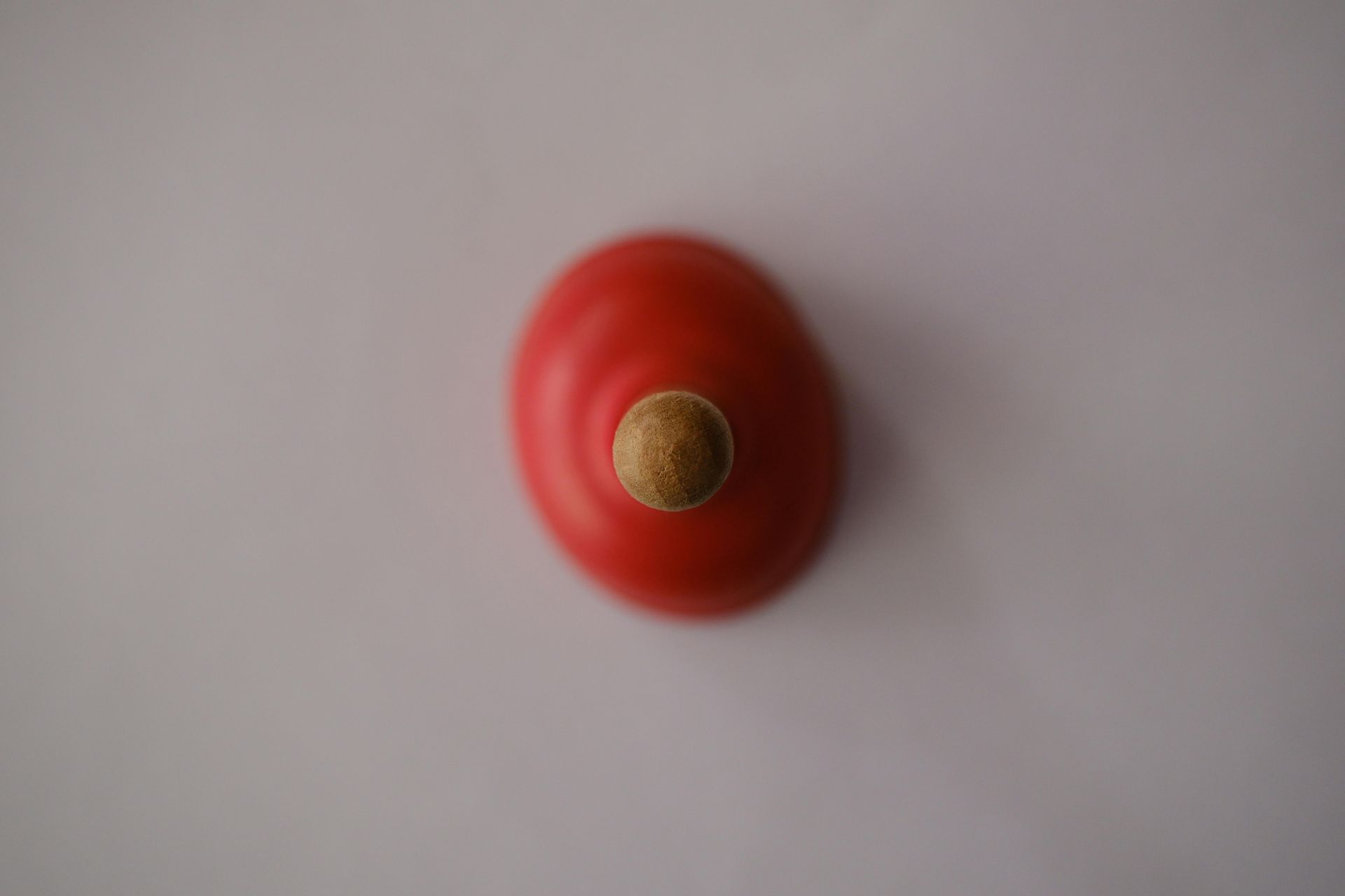 A red spinning top with a wooden handle on a white surface.