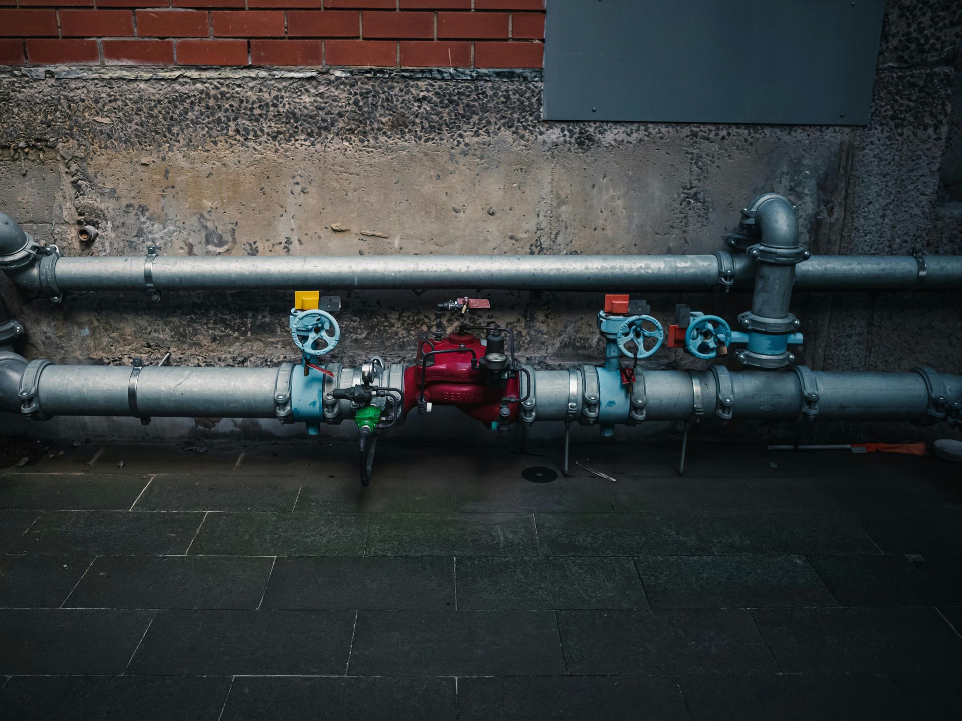 A row of pipes with valves attached to them against a brick wall.