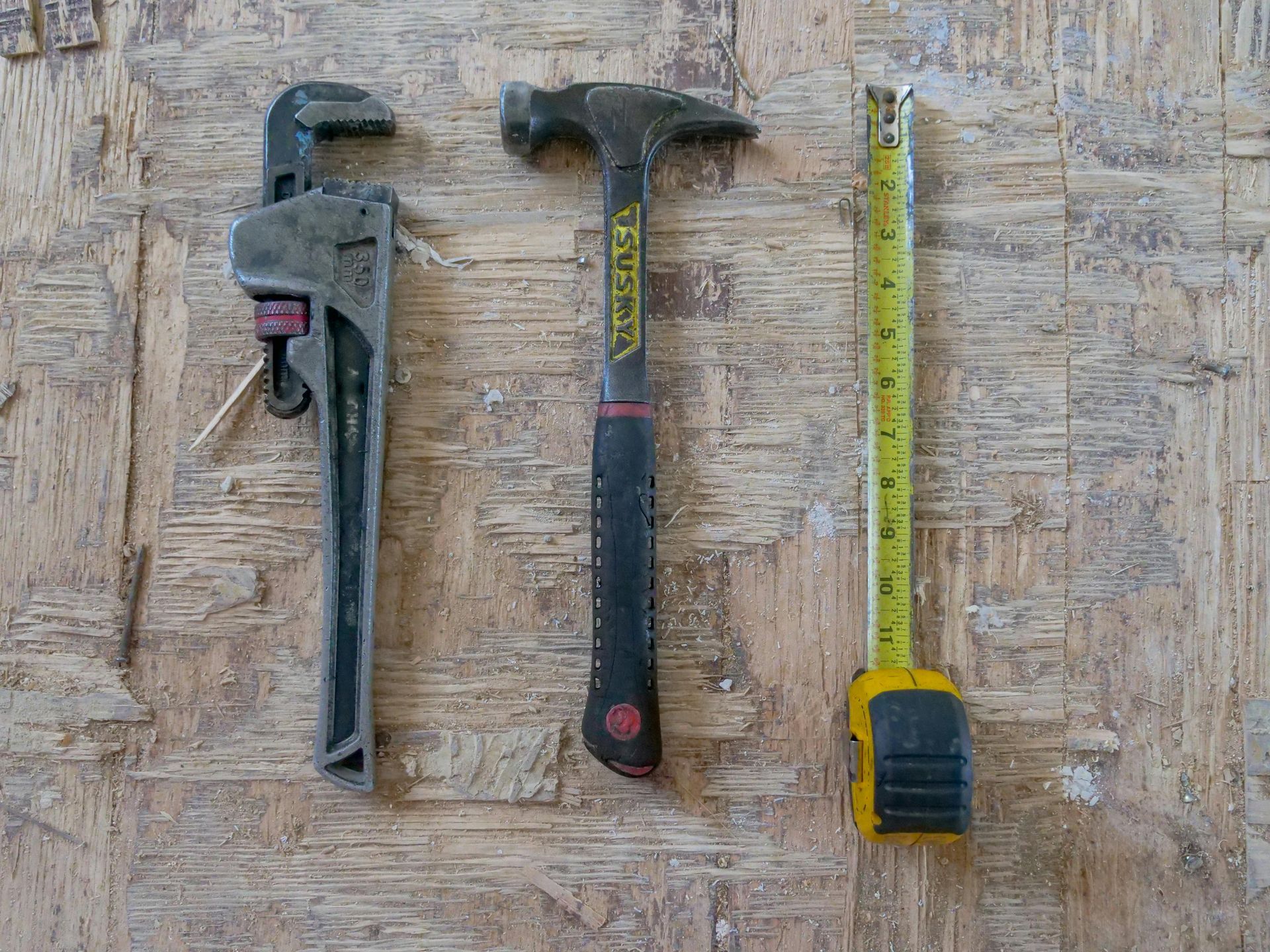 A hammer , wrench , and tape measure are sitting on a wooden table.