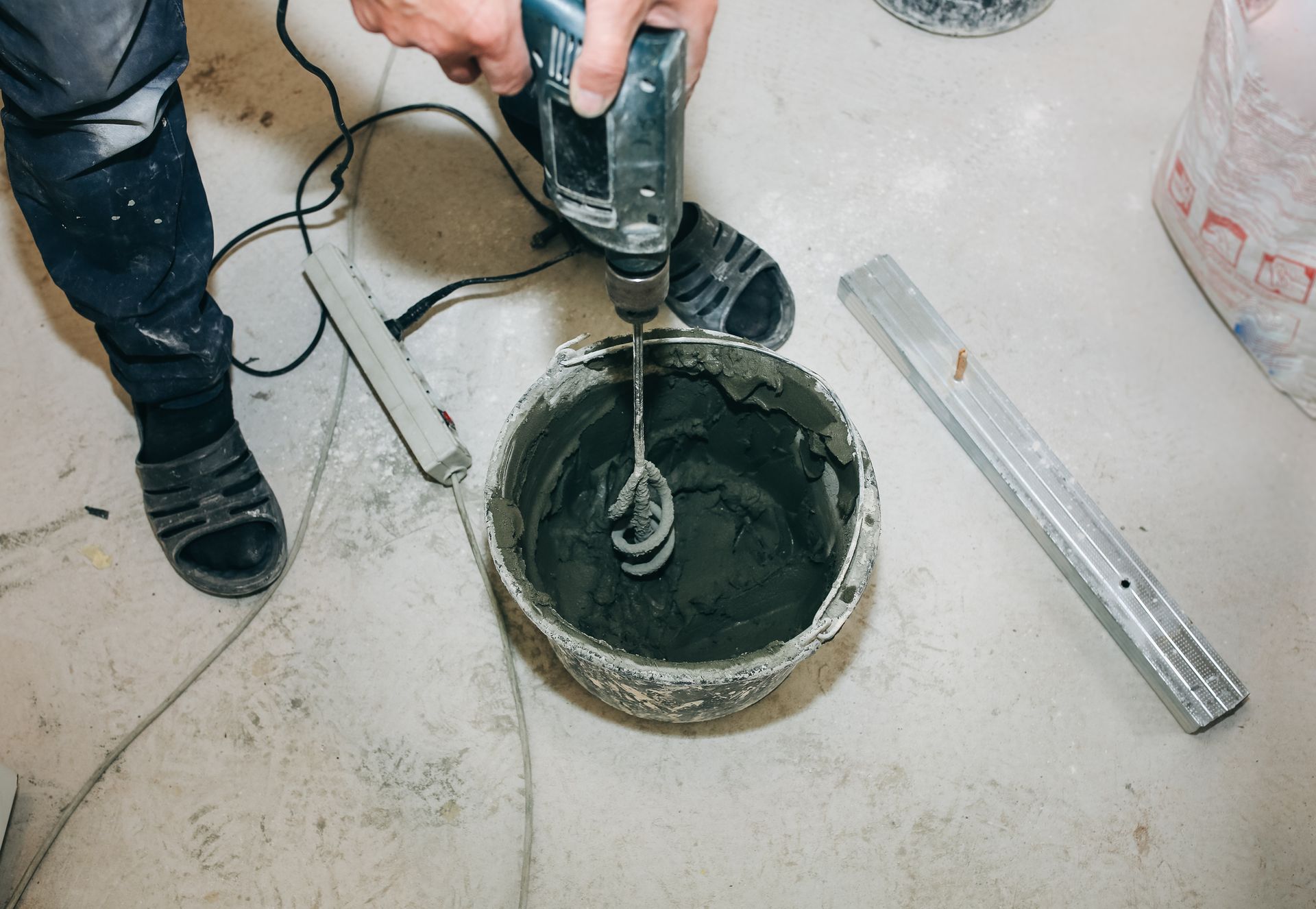 A person is mixing cement in a bowl with a drill.