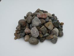 A dump truck is dumping gravel on a dirt road.