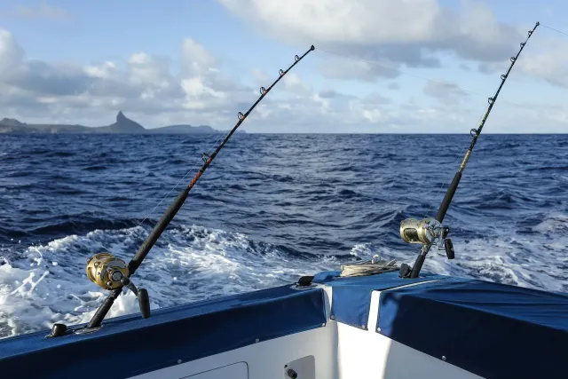 Duas varas de pesca estão na lateral de um barco no oceano.