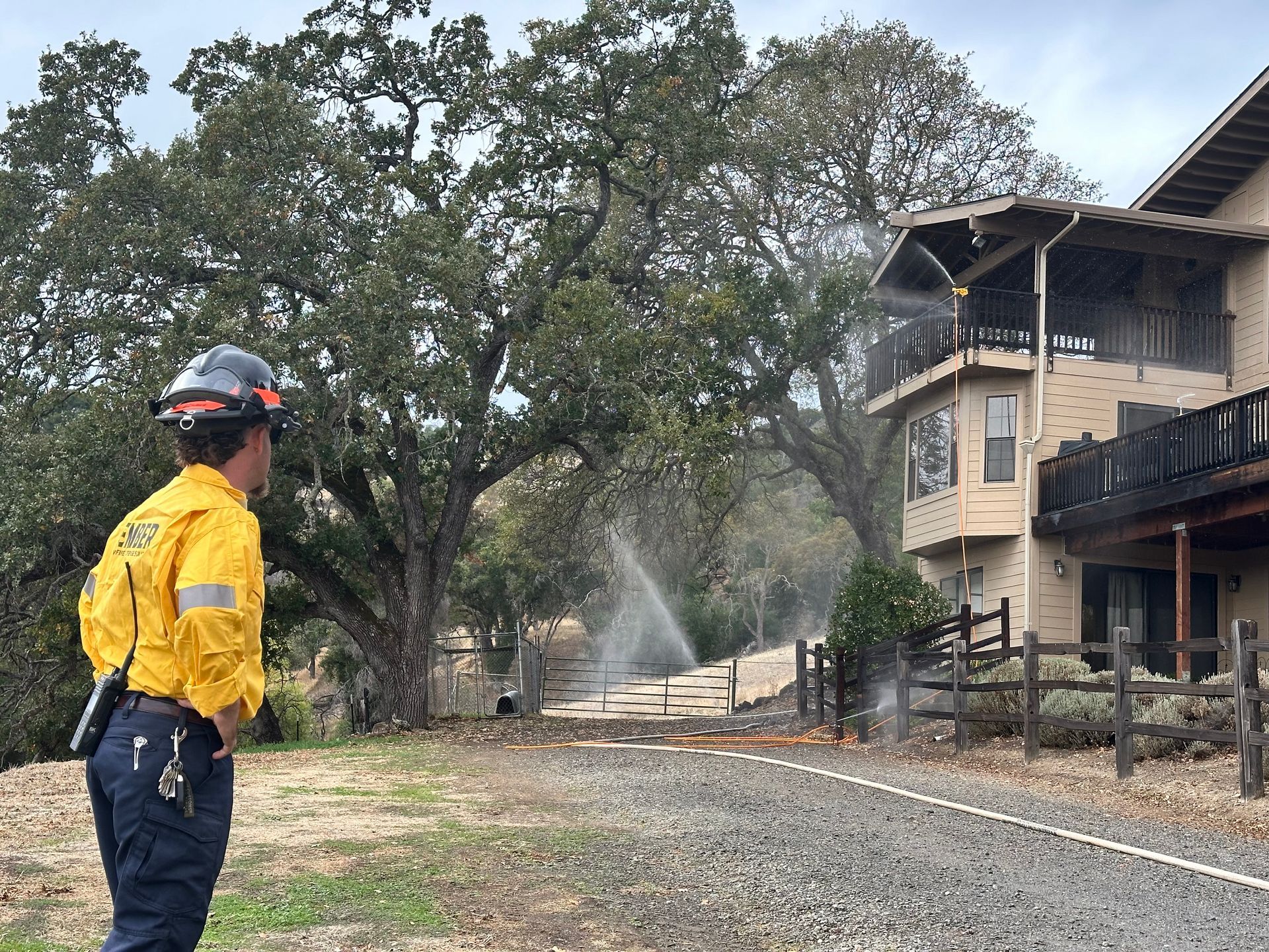 A firefighter is spraying water on a house to prevent damage from a wildfire.