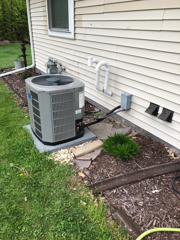 HVAC unit outside a house on a concrete pad, with ground cover of grass and mulch.