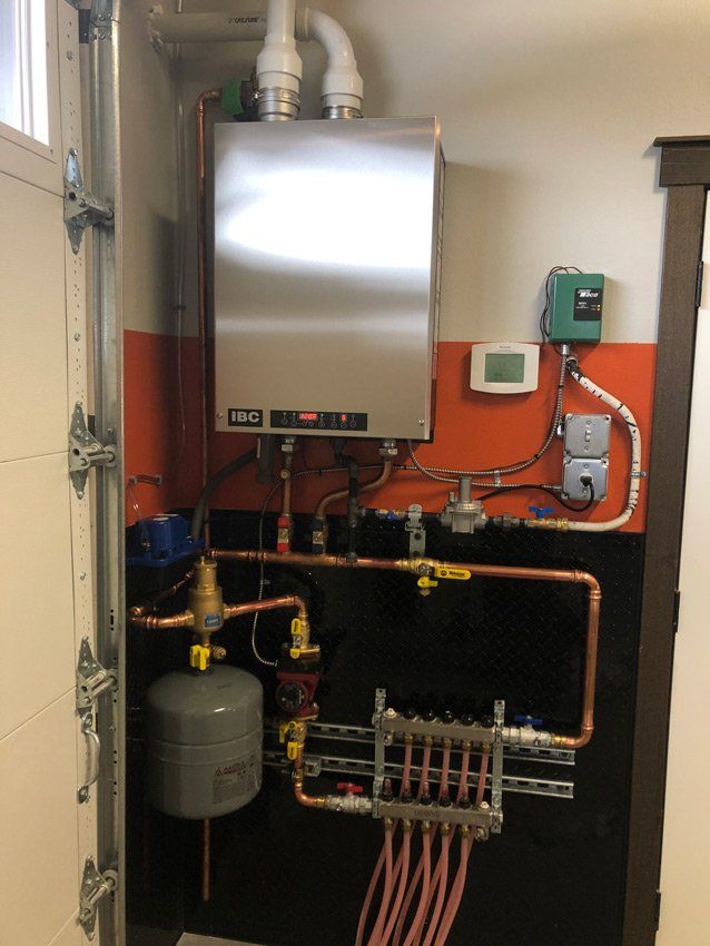 Stainless steel boiler mounted on a garage wall with copper piping and a thermostat.