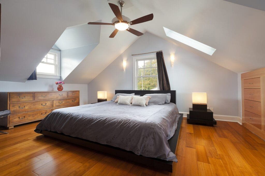 Bedroom with a slanted ceiling, wooden floors, a bed, dressers, and windows.