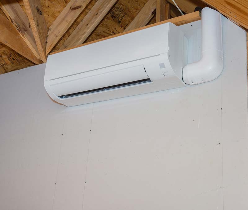 White wall-mounted ductless mini-split AC unit with a curved vent. Installed on a white wall with wooden rafters visible.