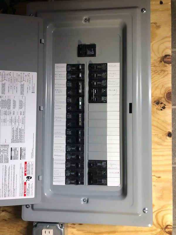 Gray electrical panel with circuit breakers on wooden wall.