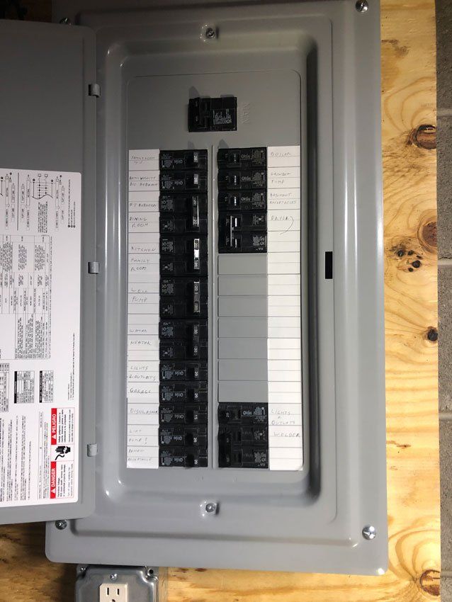 Electrical panel with circuit breakers in a gray metal box, mounted on a wood wall.