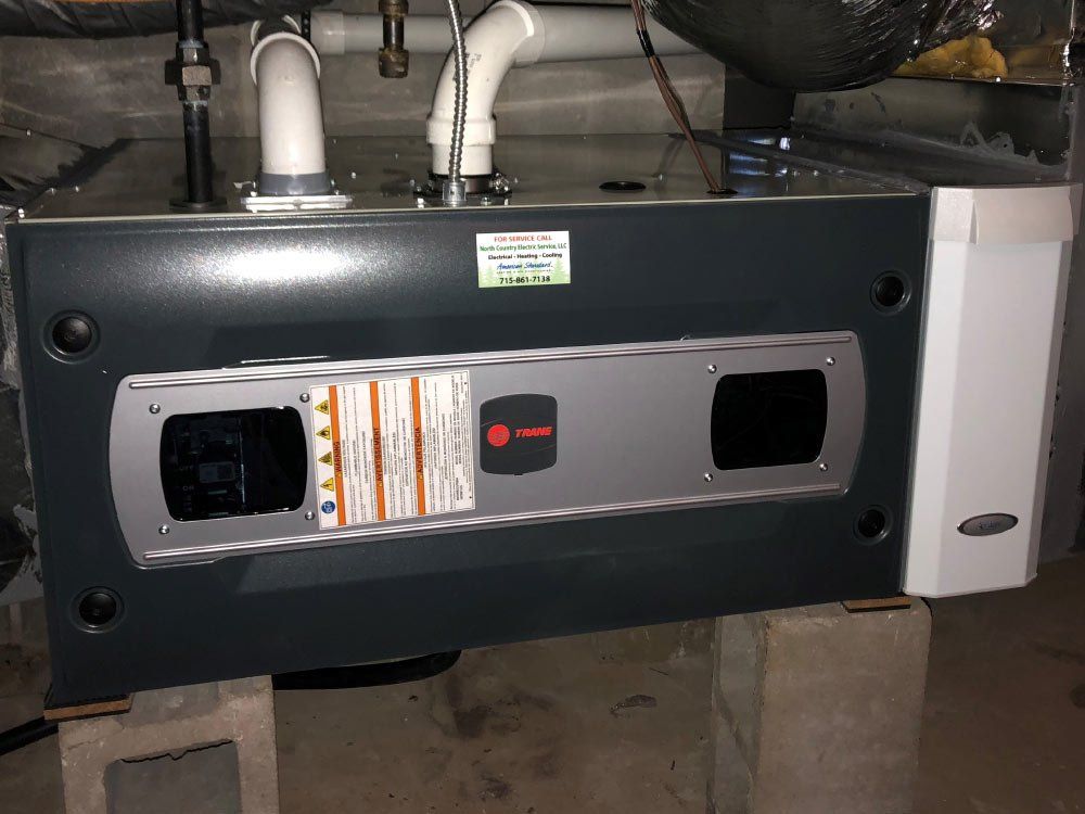 Dark gray Trane furnace on concrete blocks, with white vent pipes, in a basement.