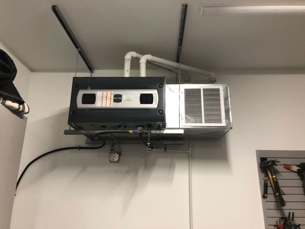 Furnace and air conditioning unit mounted on a garage wall, with white pipes and vents.