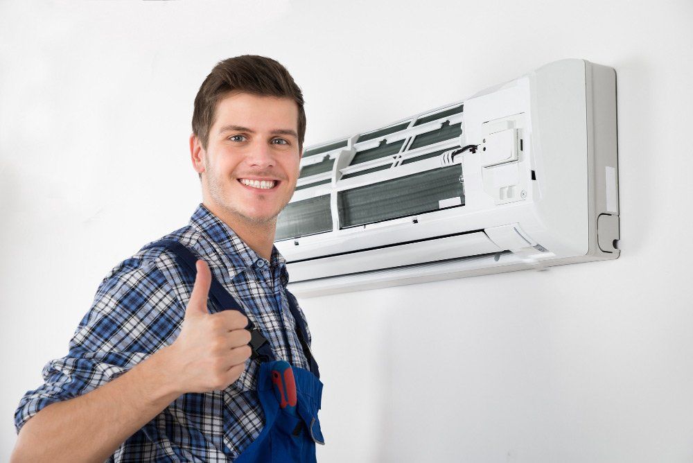 Man in blue plaid and overalls giving a thumbs up near a white air conditioner on a wall.