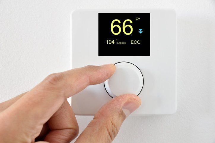 Hand turning a white thermostat dial set to 66 degrees, with an ECO setting displayed.