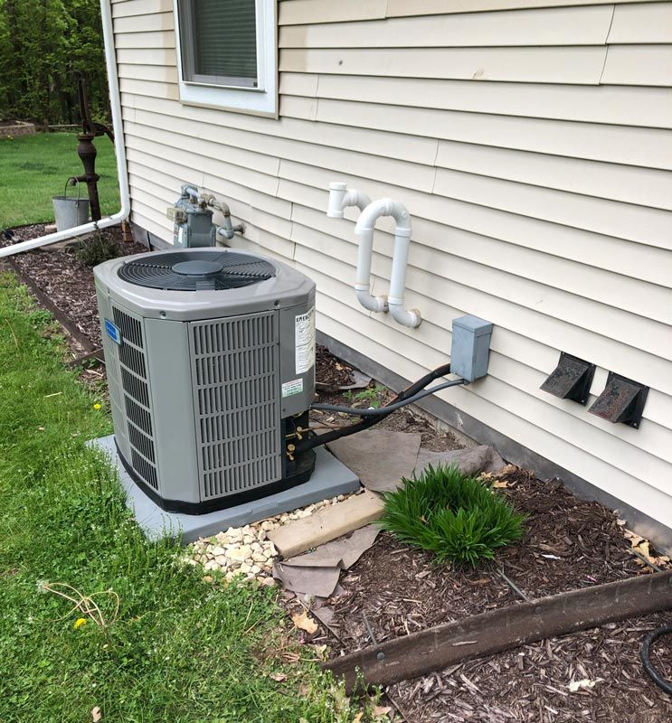 An air conditioning unit next to a beige house; green lawn and gravel around the unit.