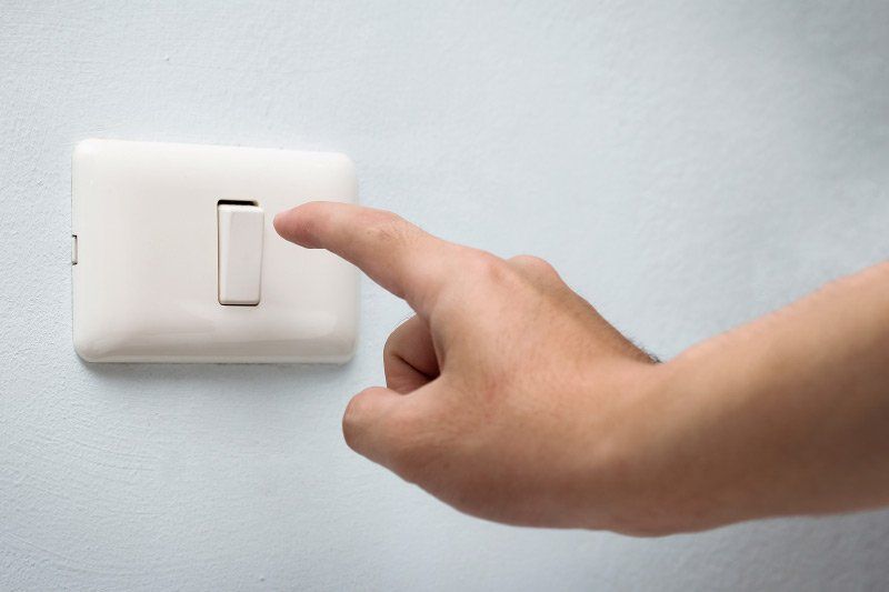 Hand pressing a white light switch on a light blue wall.