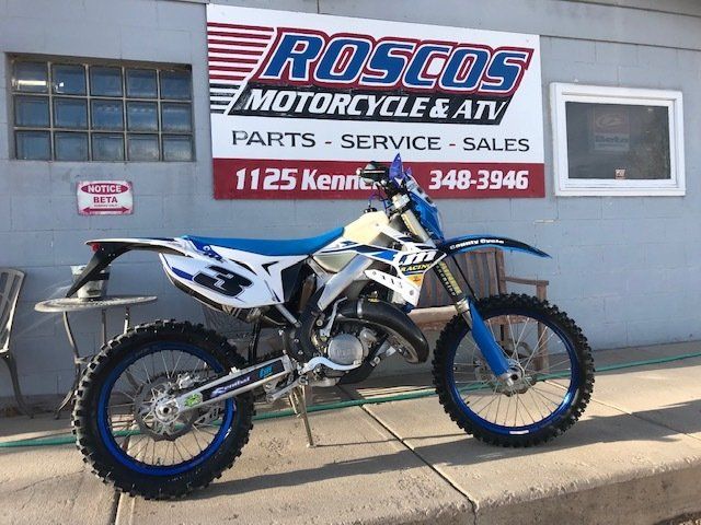 A dirt bike is parked in front of a roscos motorcycle and atv store