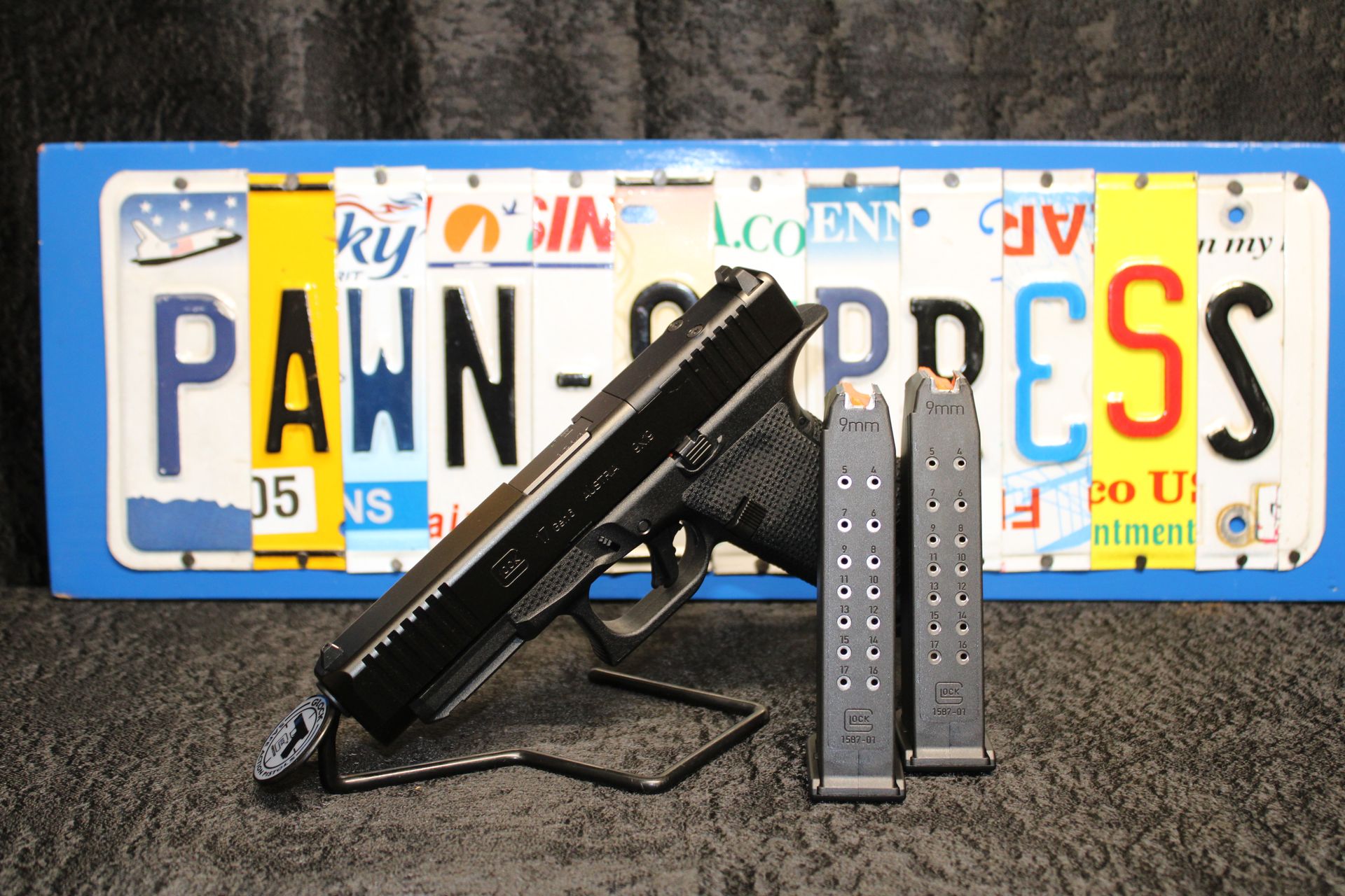Black handgun with two magazines in front of novelty license plates spelling “PAWN EXPRESS”