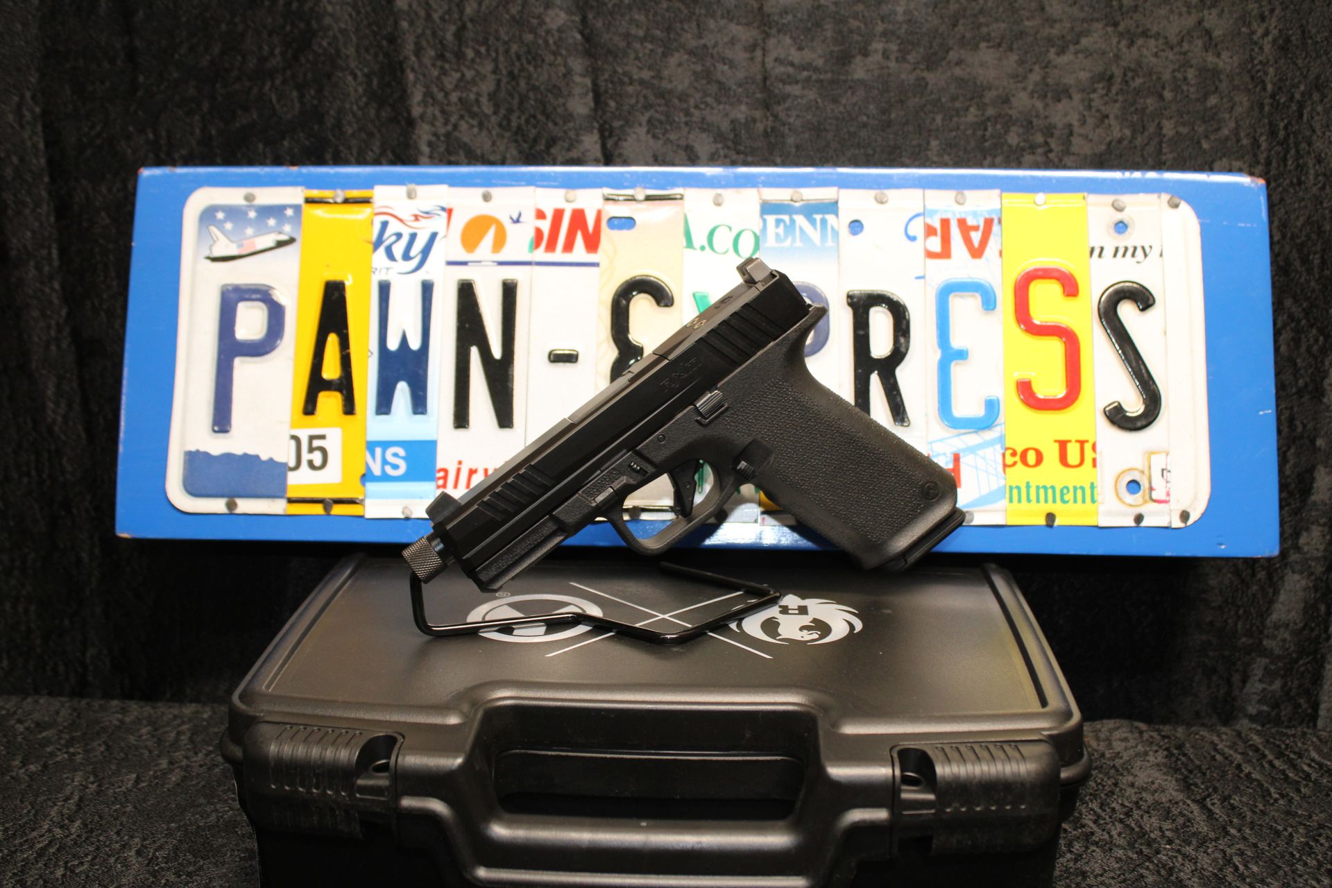 Handgun on a black case in front of a blue Pennsylvania license plate reading “PAWN-RESS”