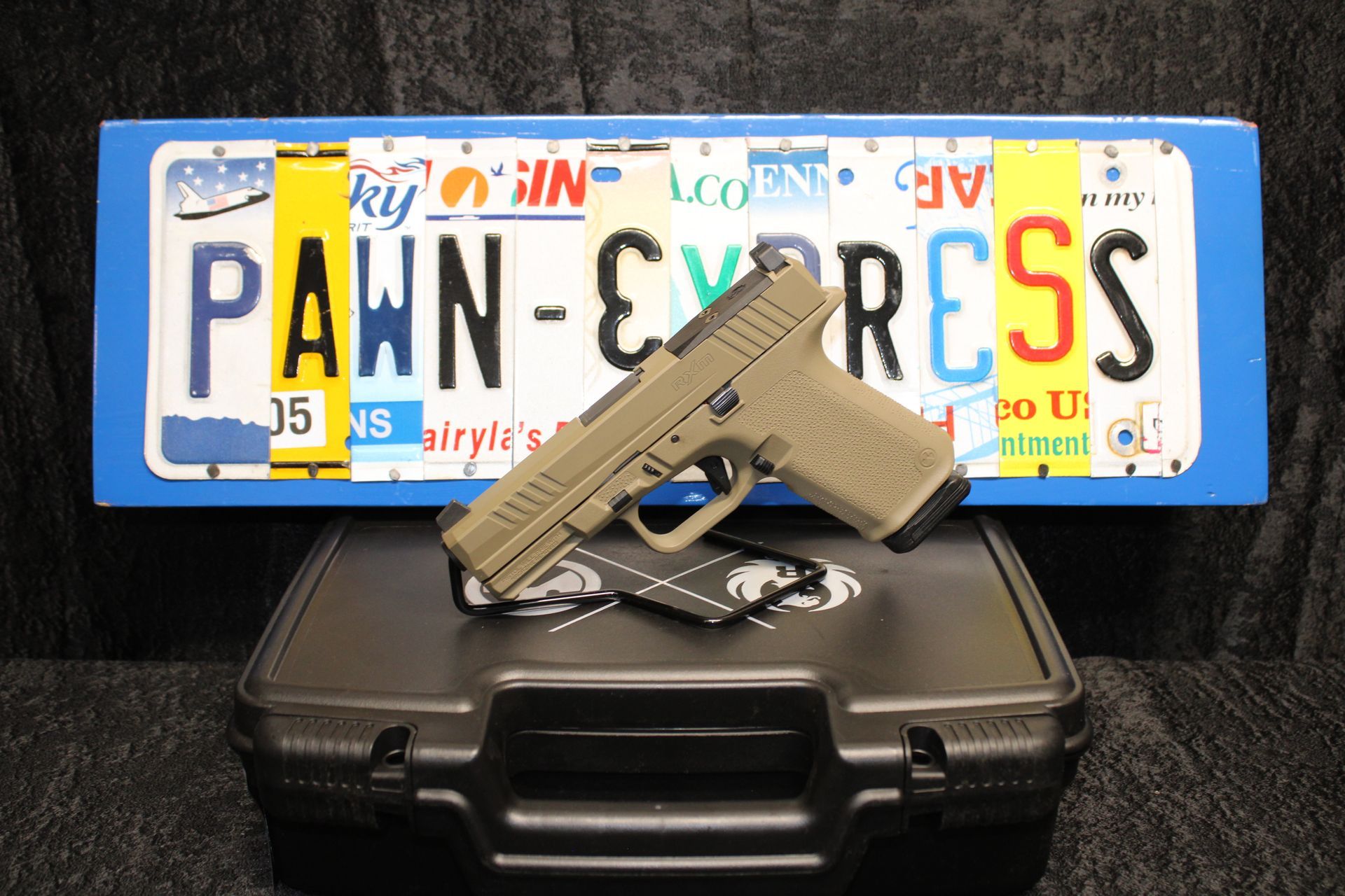 Handgun resting on a black case in front of a Pennsylvania license plate reading “PAWN-EXPRESS.”