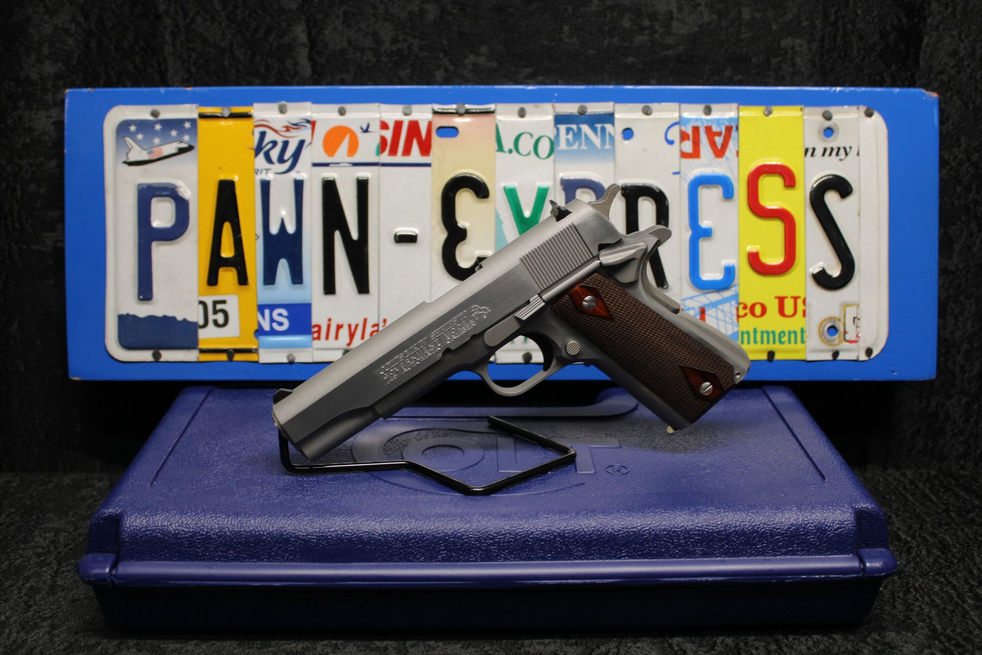 Handgun resting on a blue case in front of a blue license plate reading “PAWN-EXPRESS”
