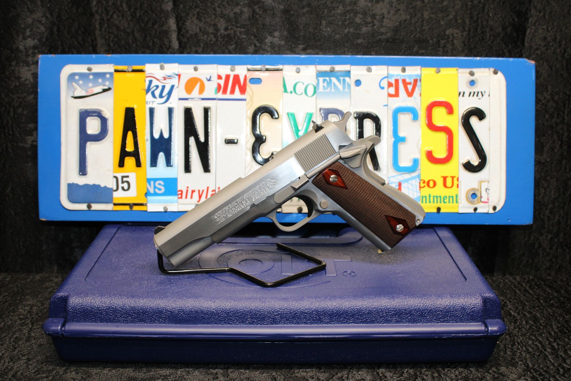 Two handguns displayed on a blue case in front of a license plate reading “PAWN-GRESS”