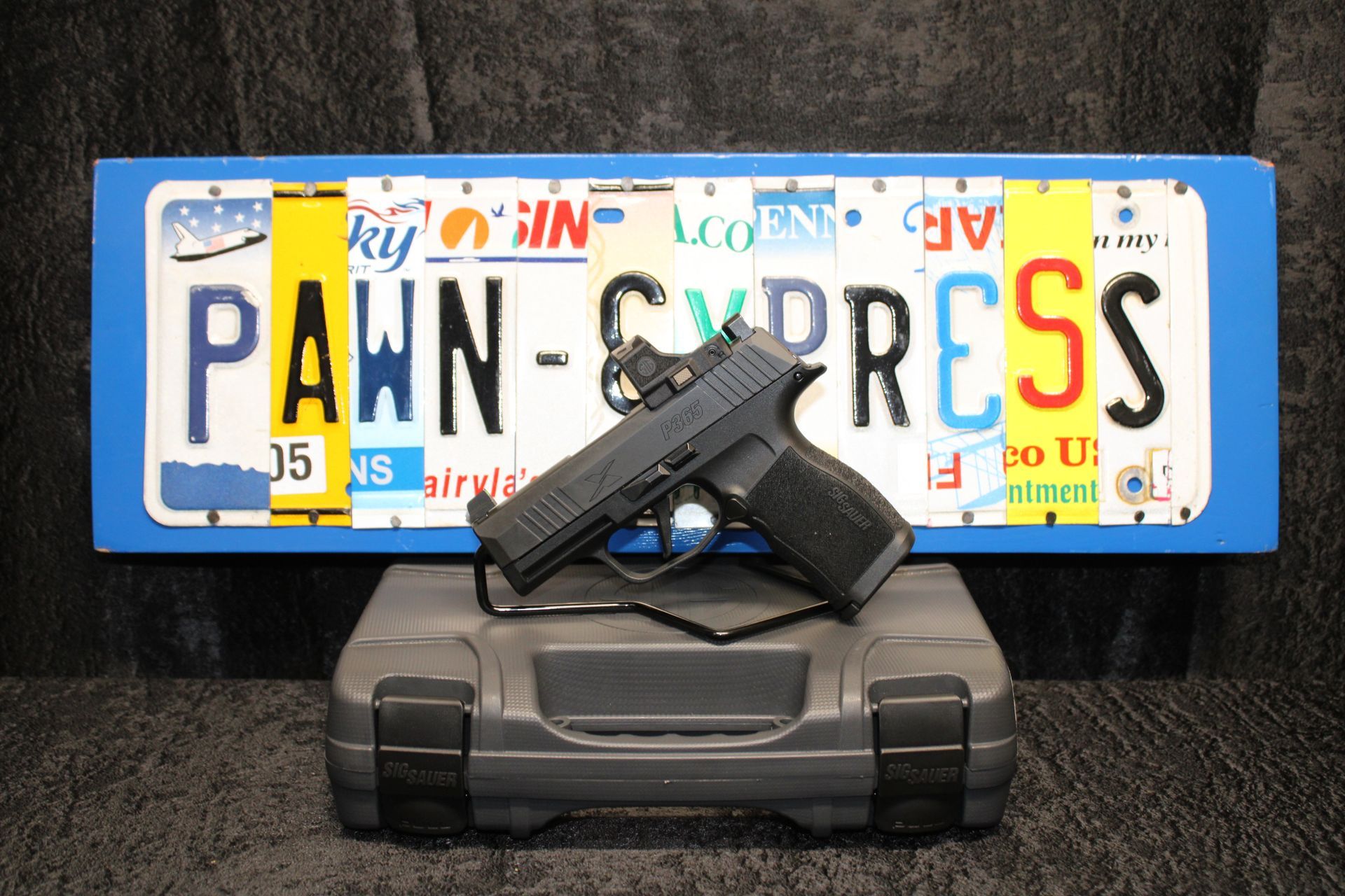 Handgun in front of a Pennsylvania “PAWN” license plate on a black case