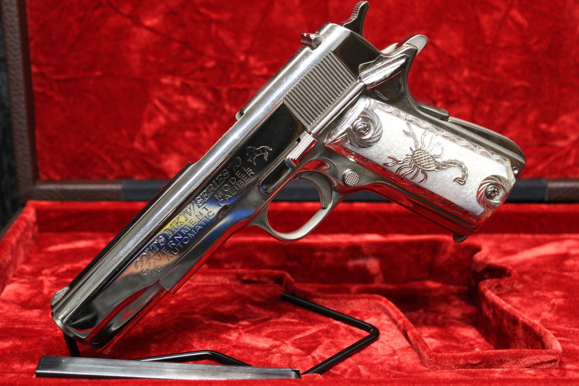 Decorative silver handgun with engraved grip displayed on a red velvet stand