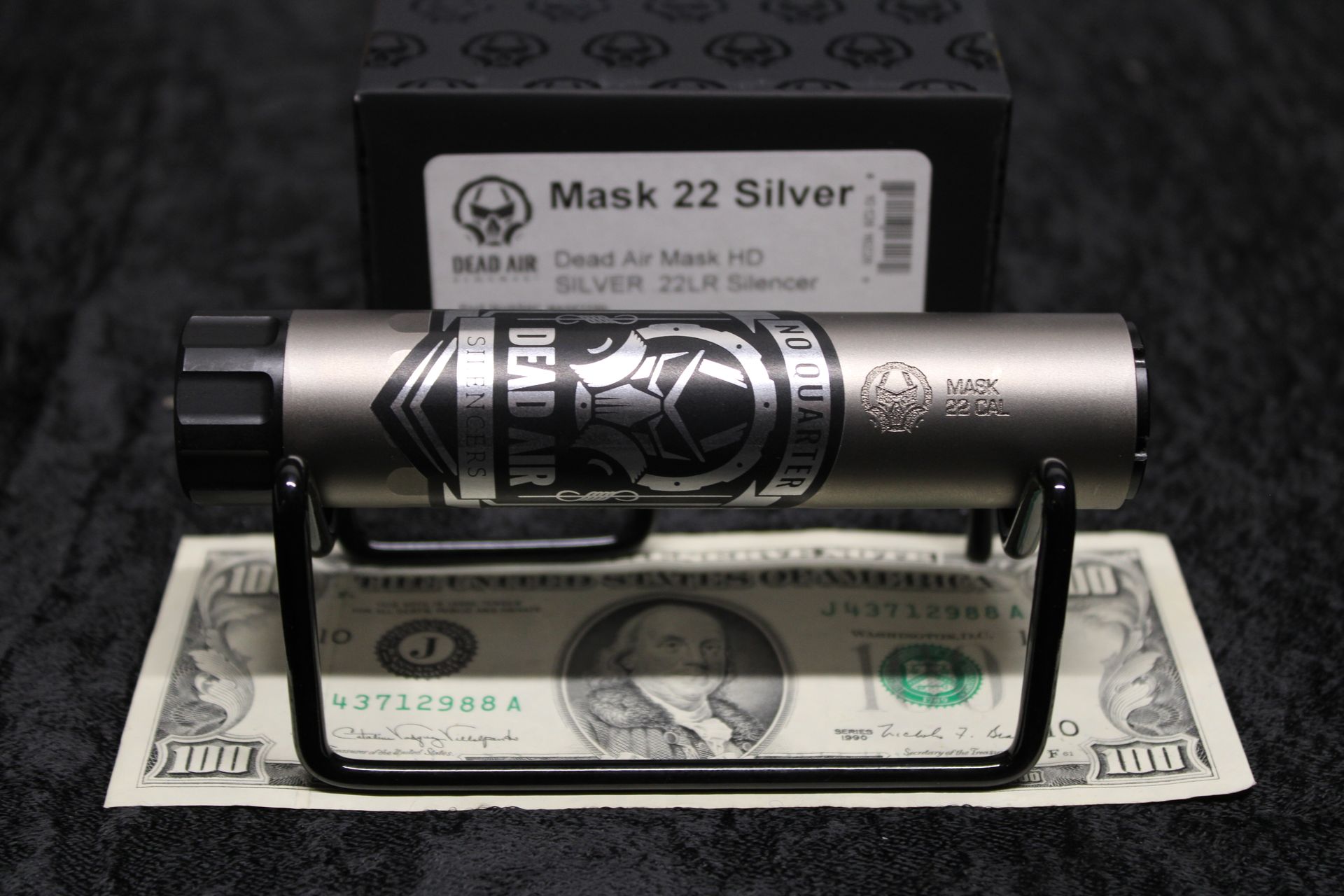 Silver flashlight on a stand with a $100 bill and its box behind it on a dark surface