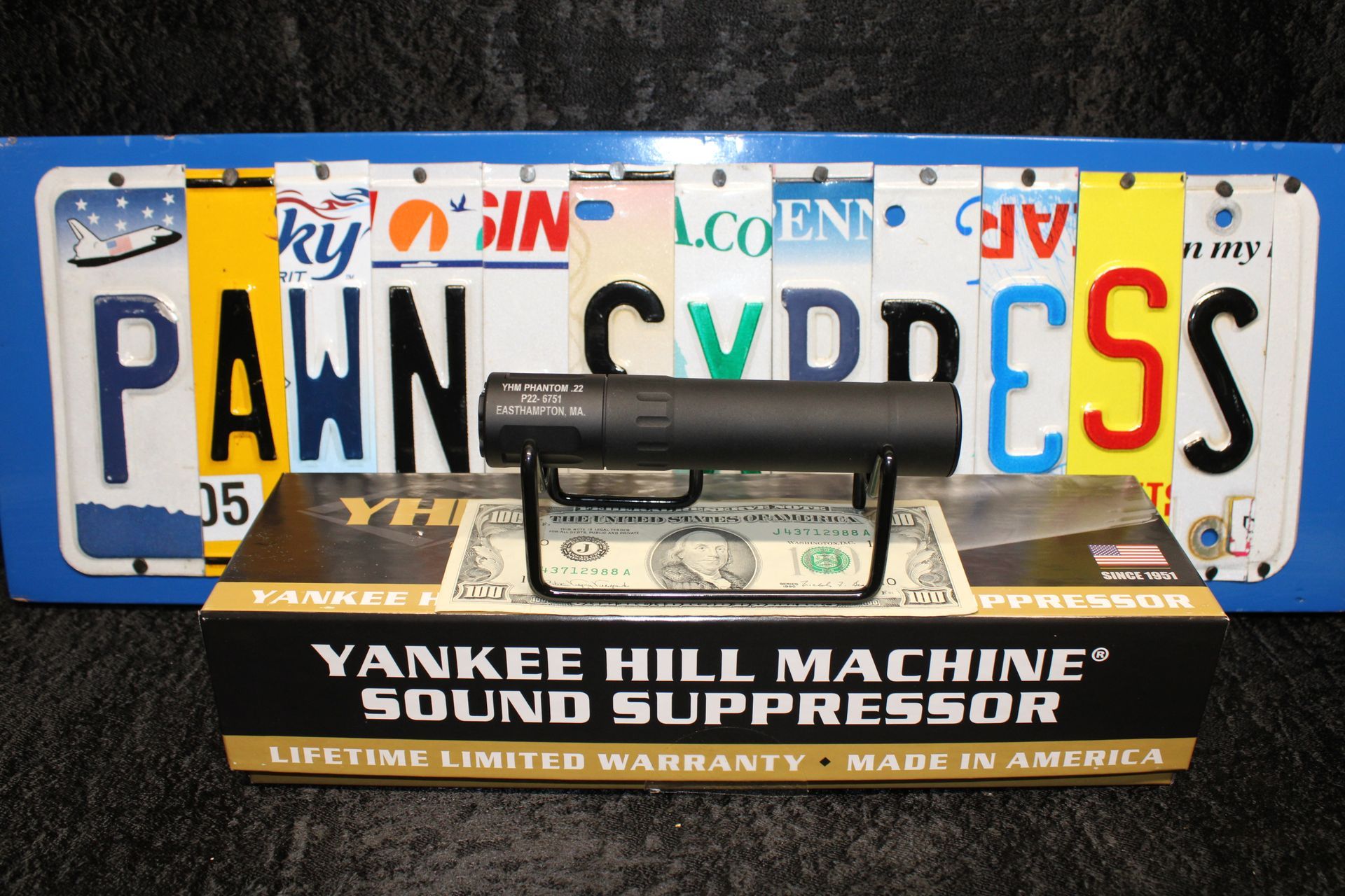 Yankee Hill Machine sound suppressor displayed in front of colorful license plates and a Pennsylvania plate.