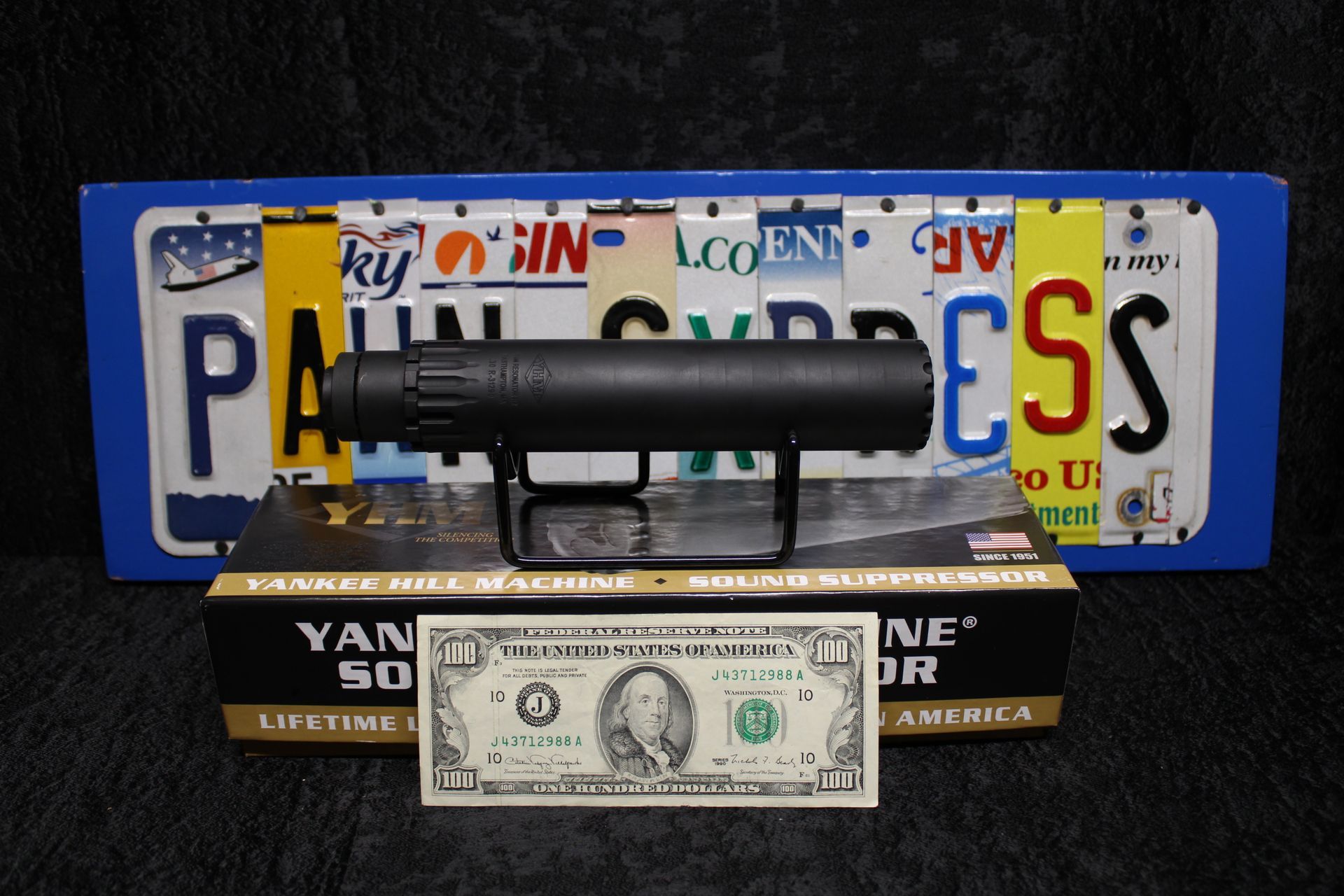 Black pistol on a stand in front of a license plate and a one-dollar bill