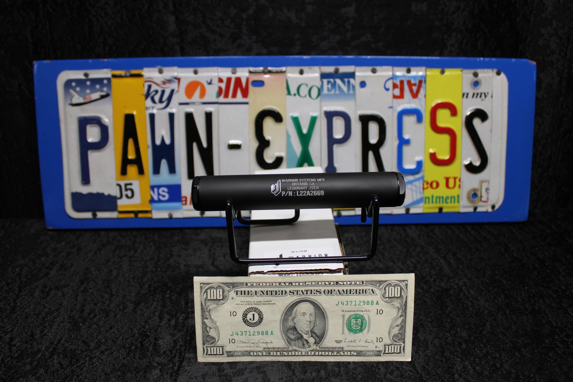 Blue Pennsylvania novelty license plate with “PAWN-CYPRSS” above a dollar bill on black stand