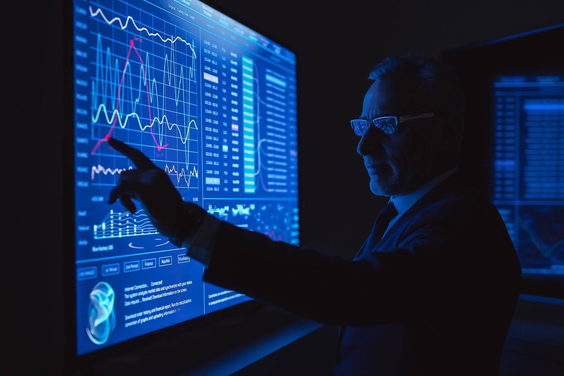 Homem apontando para dados em uma grande tela de computador azul em uma sala escura.