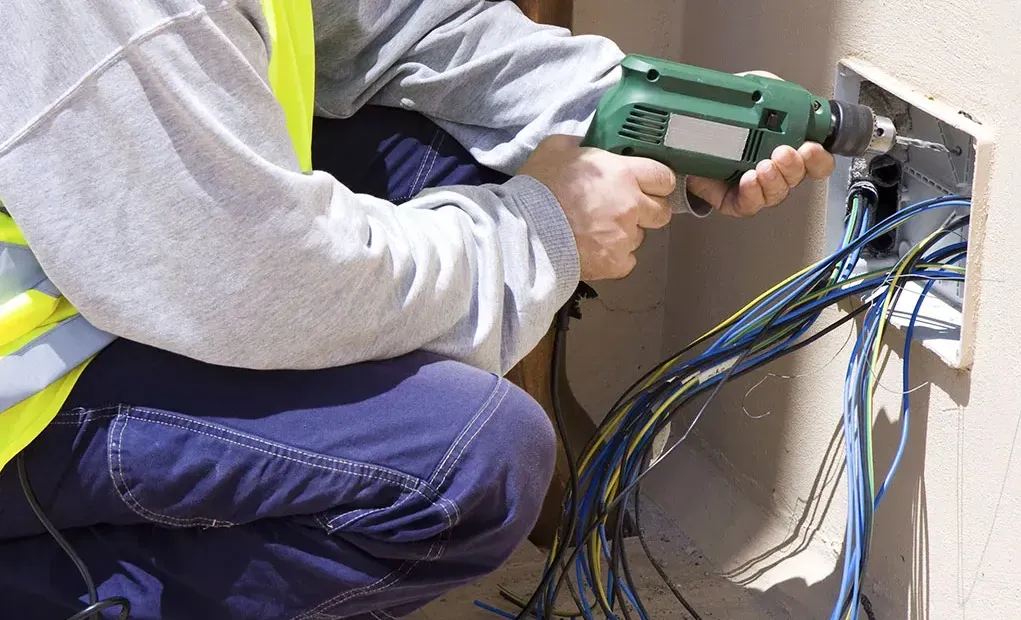 A man is using a drill to fix an electrical outlet.