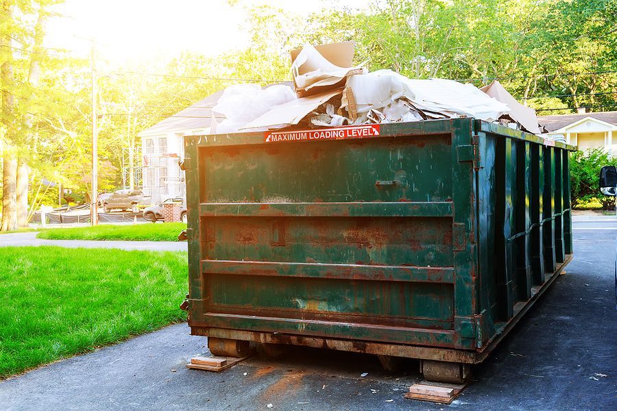 A large green dumpster is sitting in a driveway next to a house.