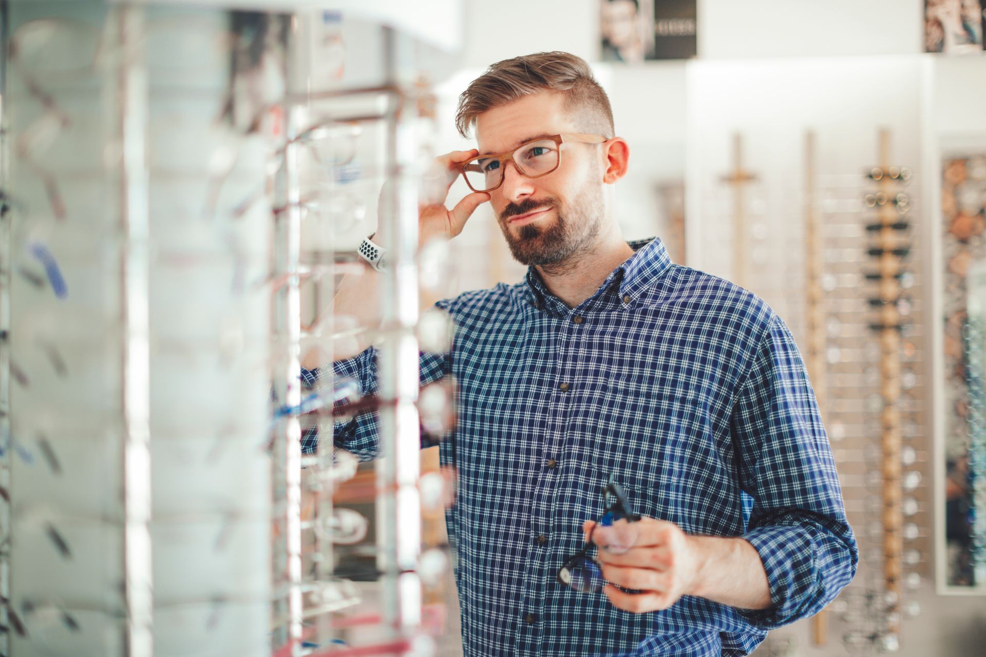 Man trying on eyeglasses at an optical shop, looking in mirror.