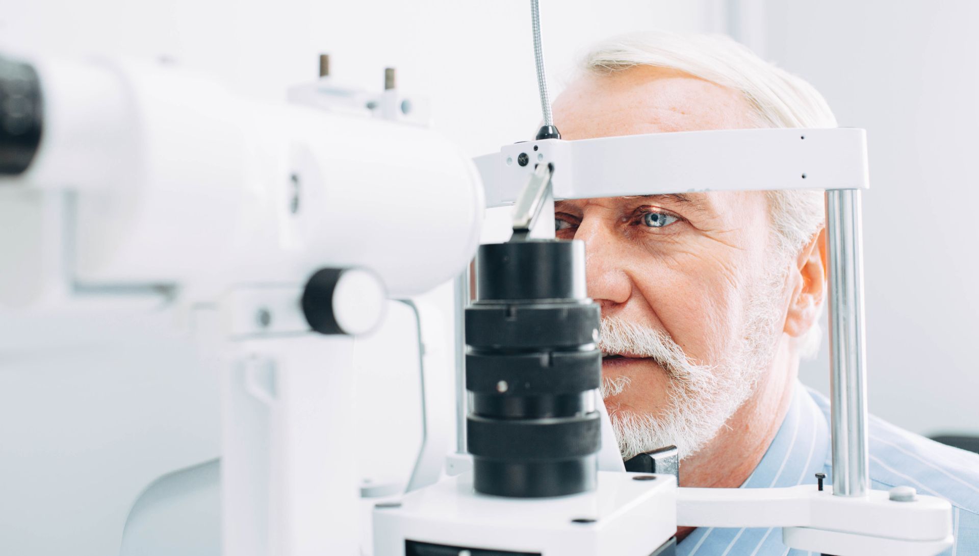 Man having an eye exam with a slit lamp machine; indoors, focused look.
