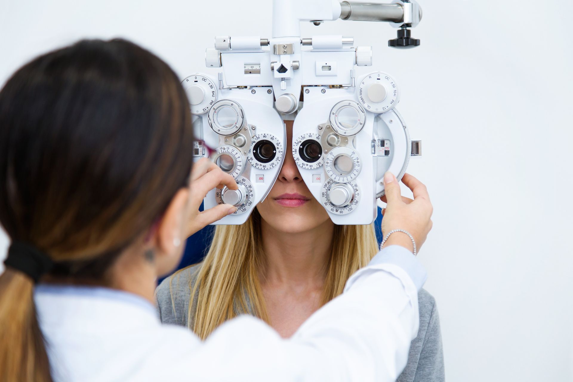 Optometrist performing an eye exam with a phoropter on a patient in a medical office.