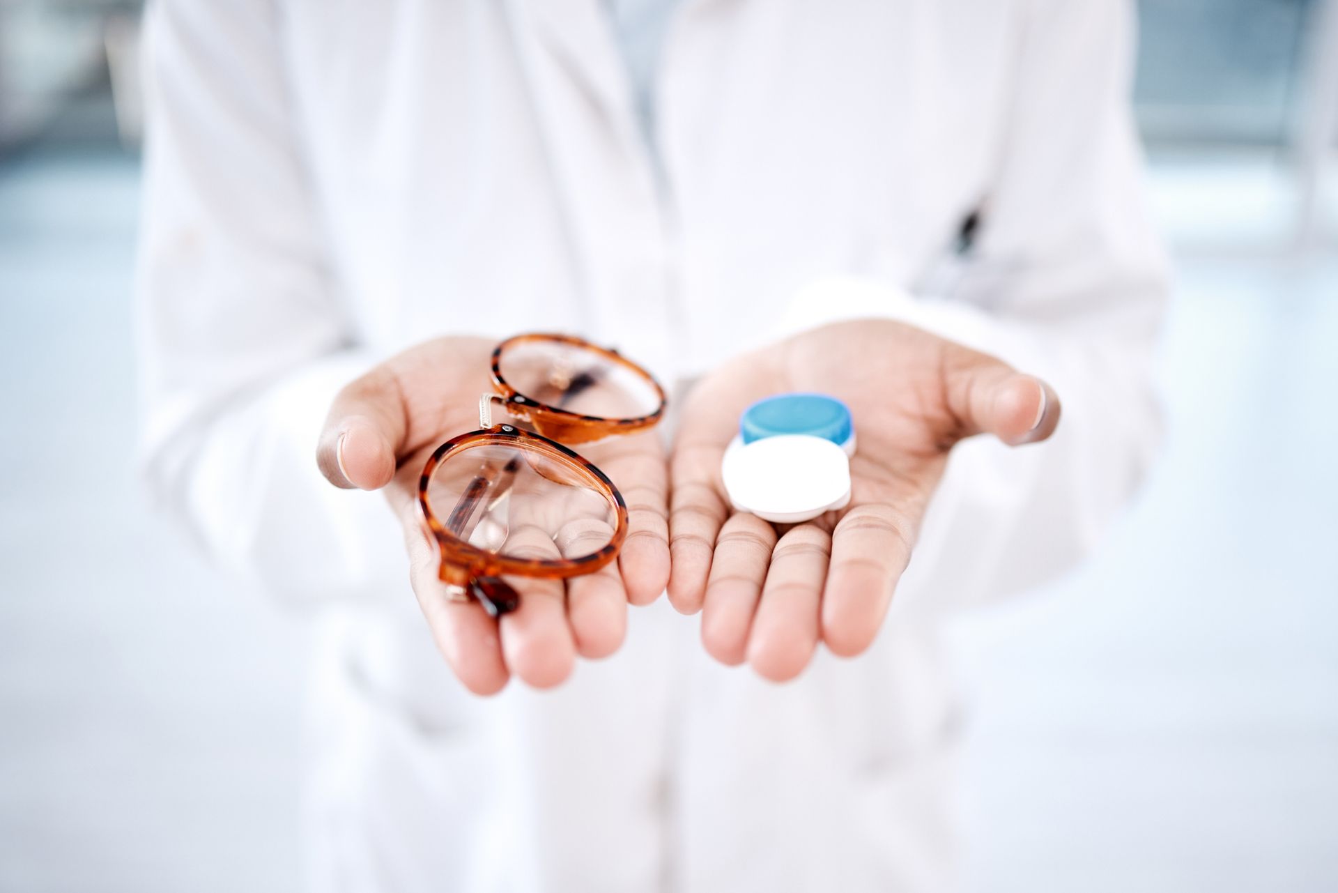 Person holding glasses in one hand and contact lens case in the other, both options for vision correction.