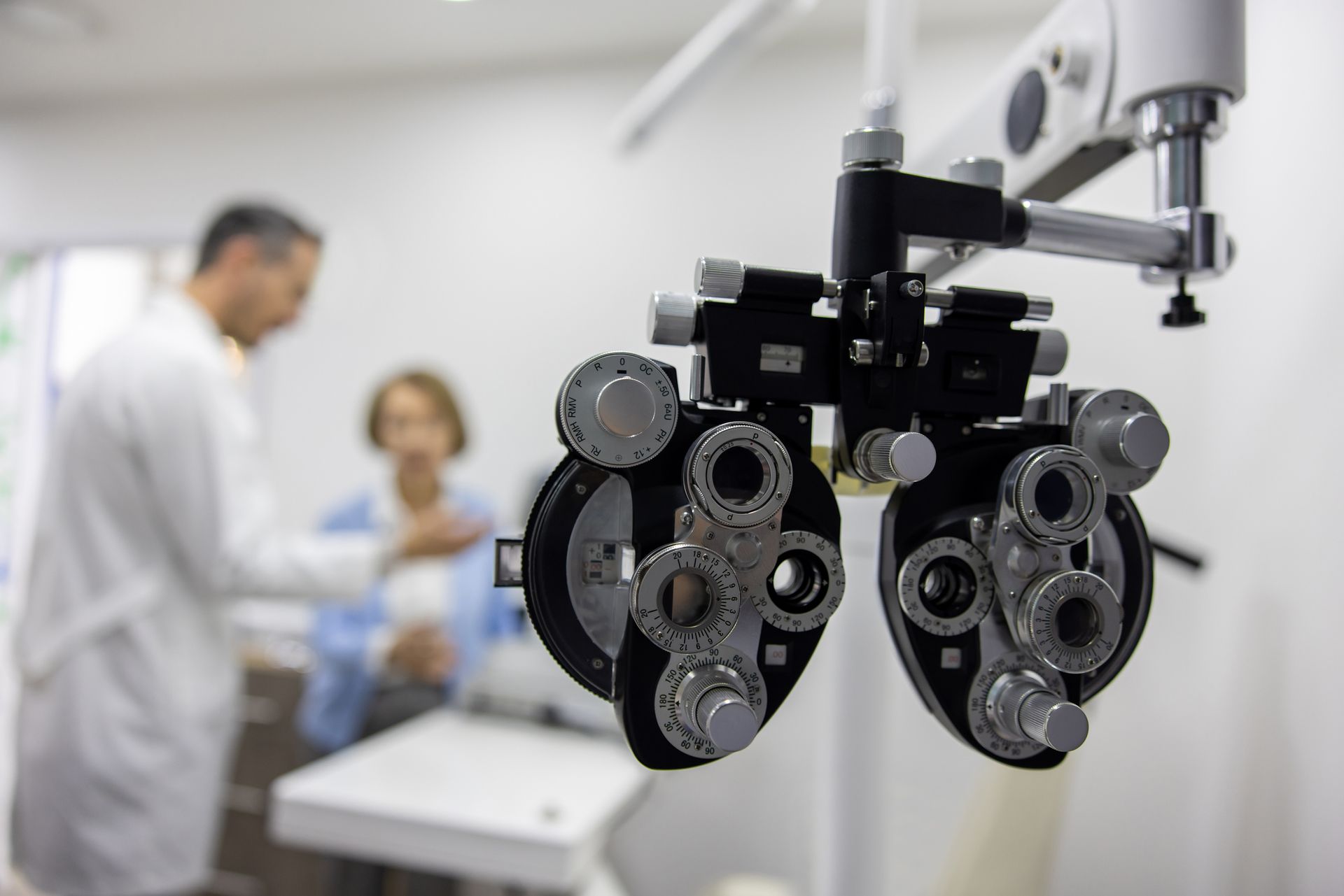 Eye exam equipment in foreground, doctor and patient blurred in background.