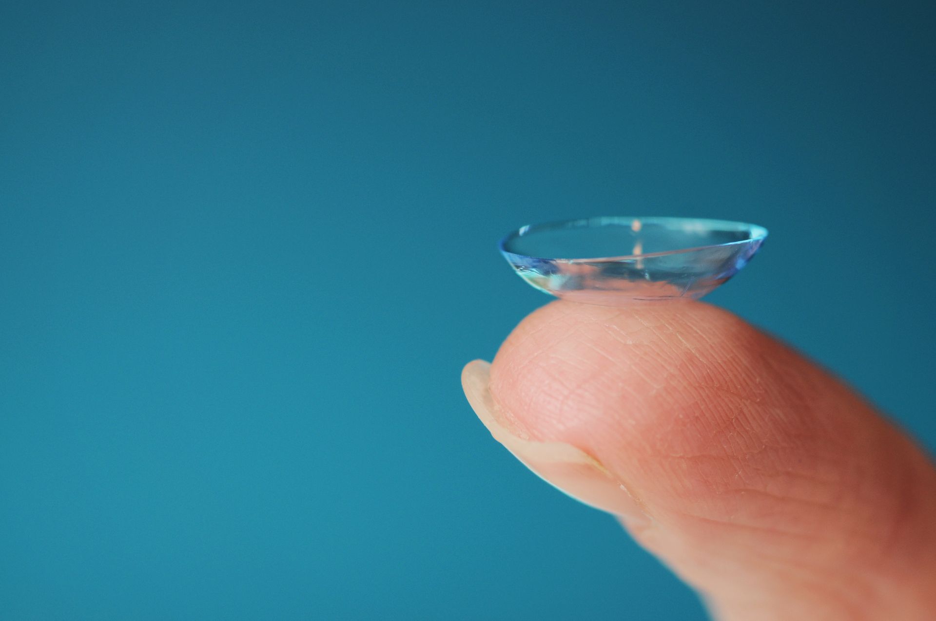 Contact lens on a fingertip against a blue background.