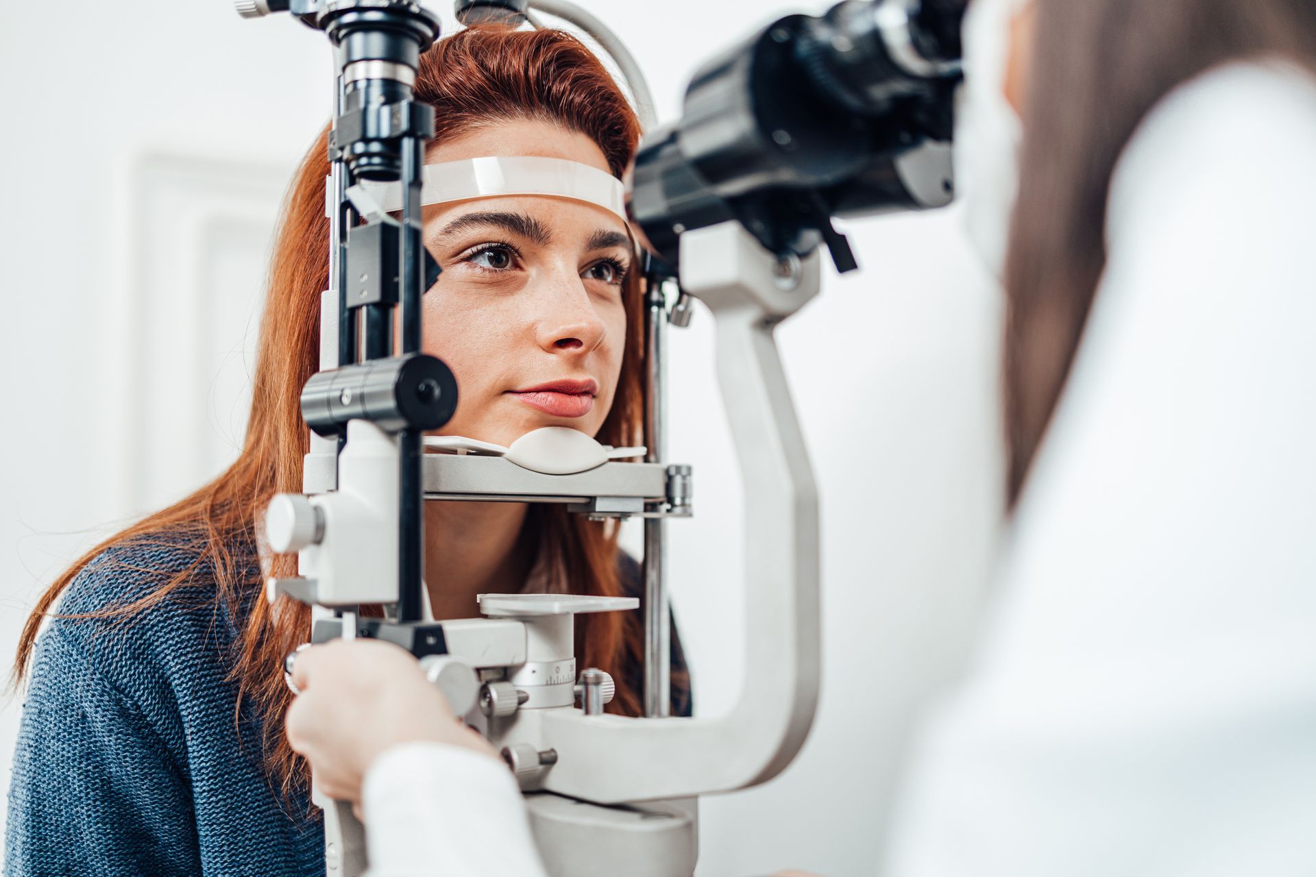 Woman having her eyes examined with a slit lamp by an eye doctor in an exam room.