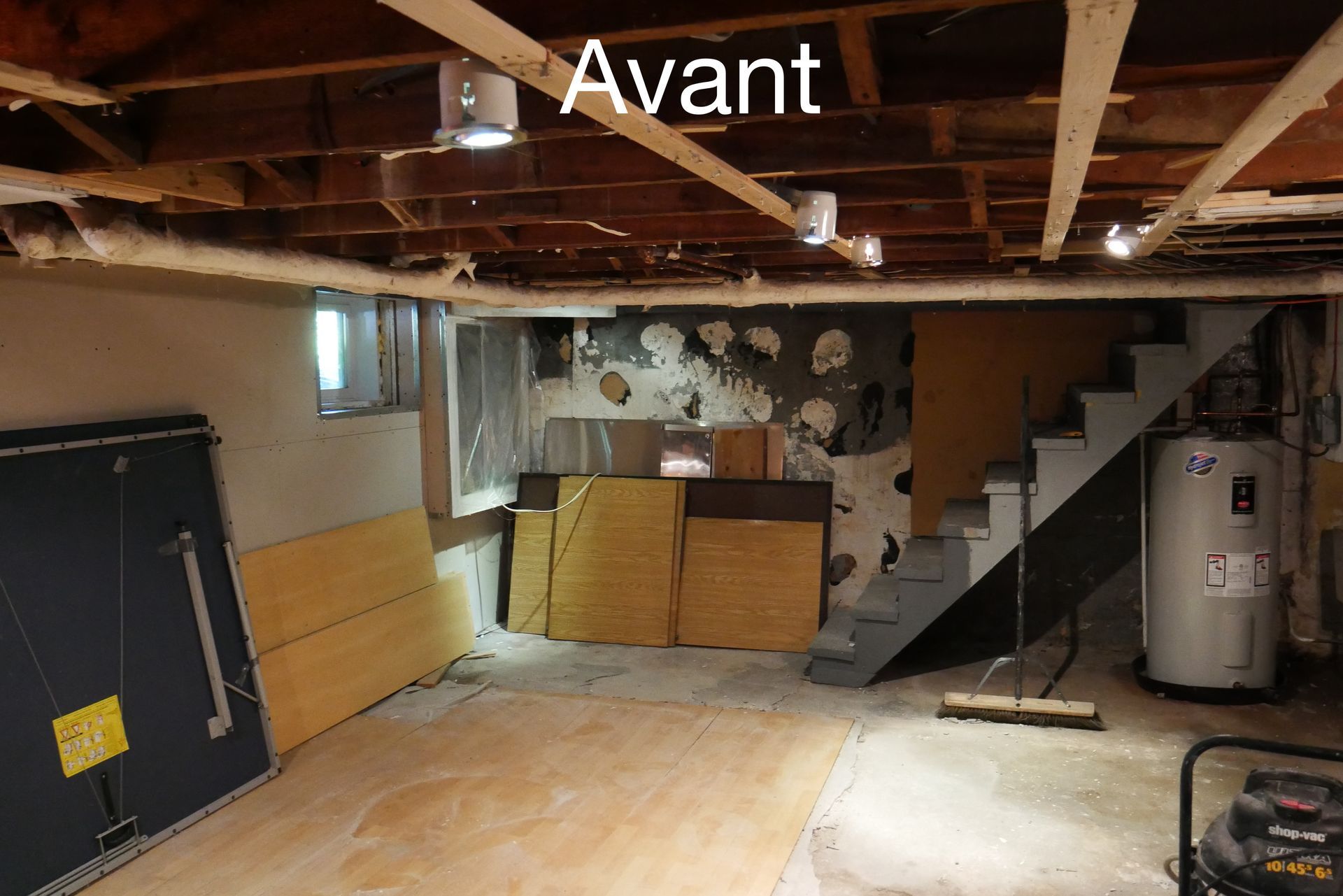 Un sous-sol avec un chauffe-eau et des escaliers et le mot avant au plafond