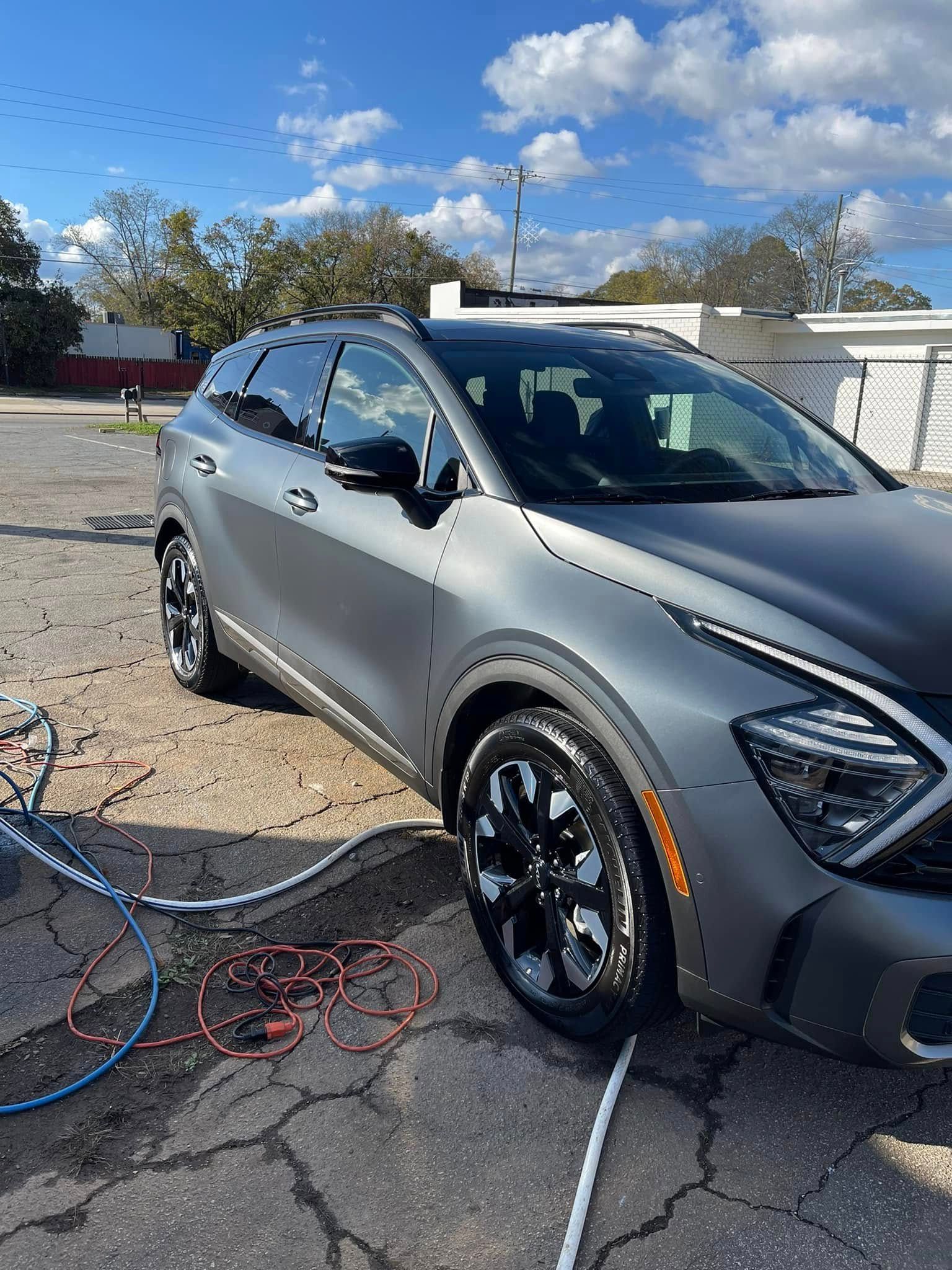 Gray SUV parked on a paved surface; blue hose on ground; sunny day.
