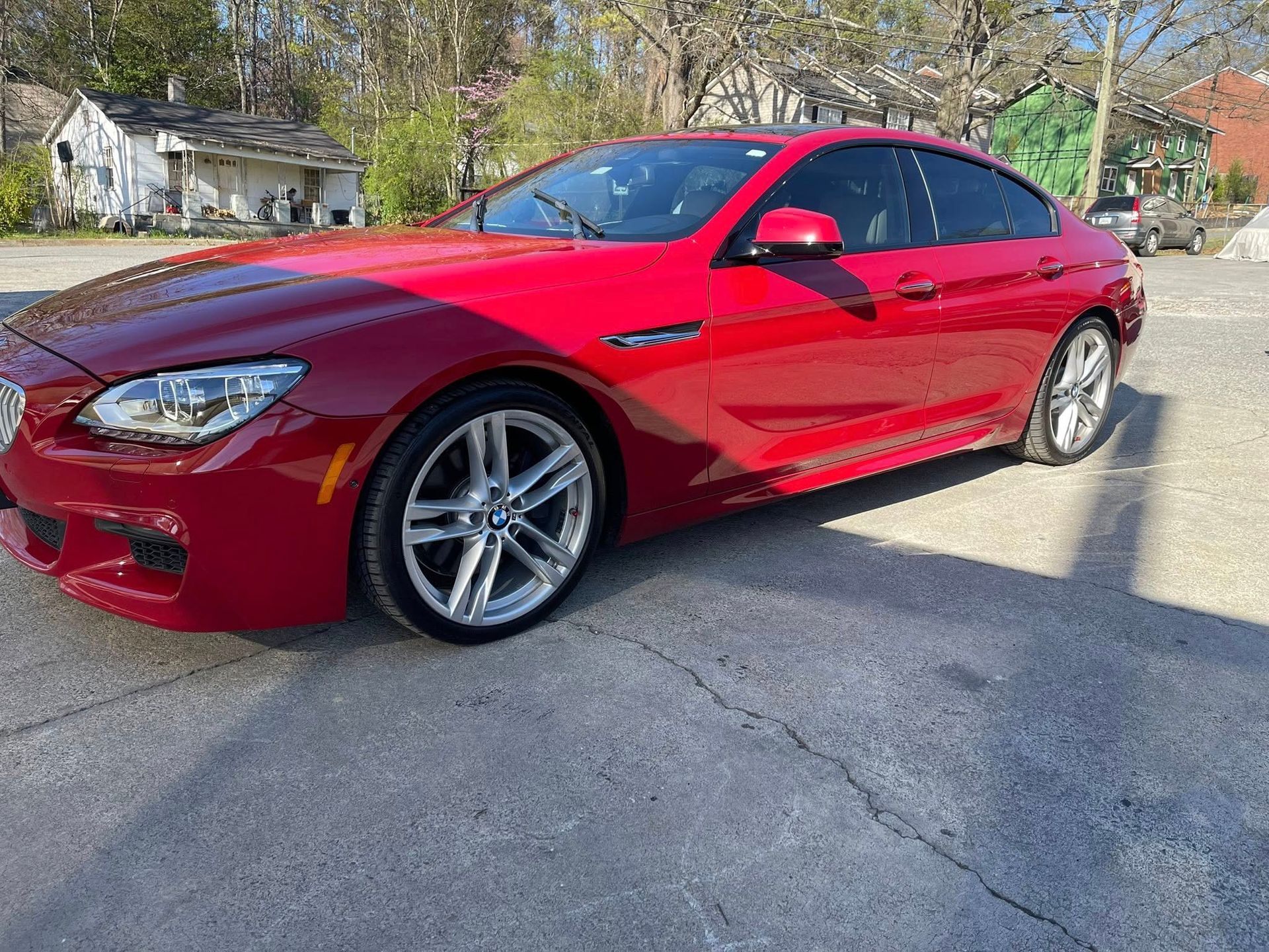 Red BMW 6 Series Gran Coupe parked on asphalt.  Bright sunlight,  in front of buildings and trees.